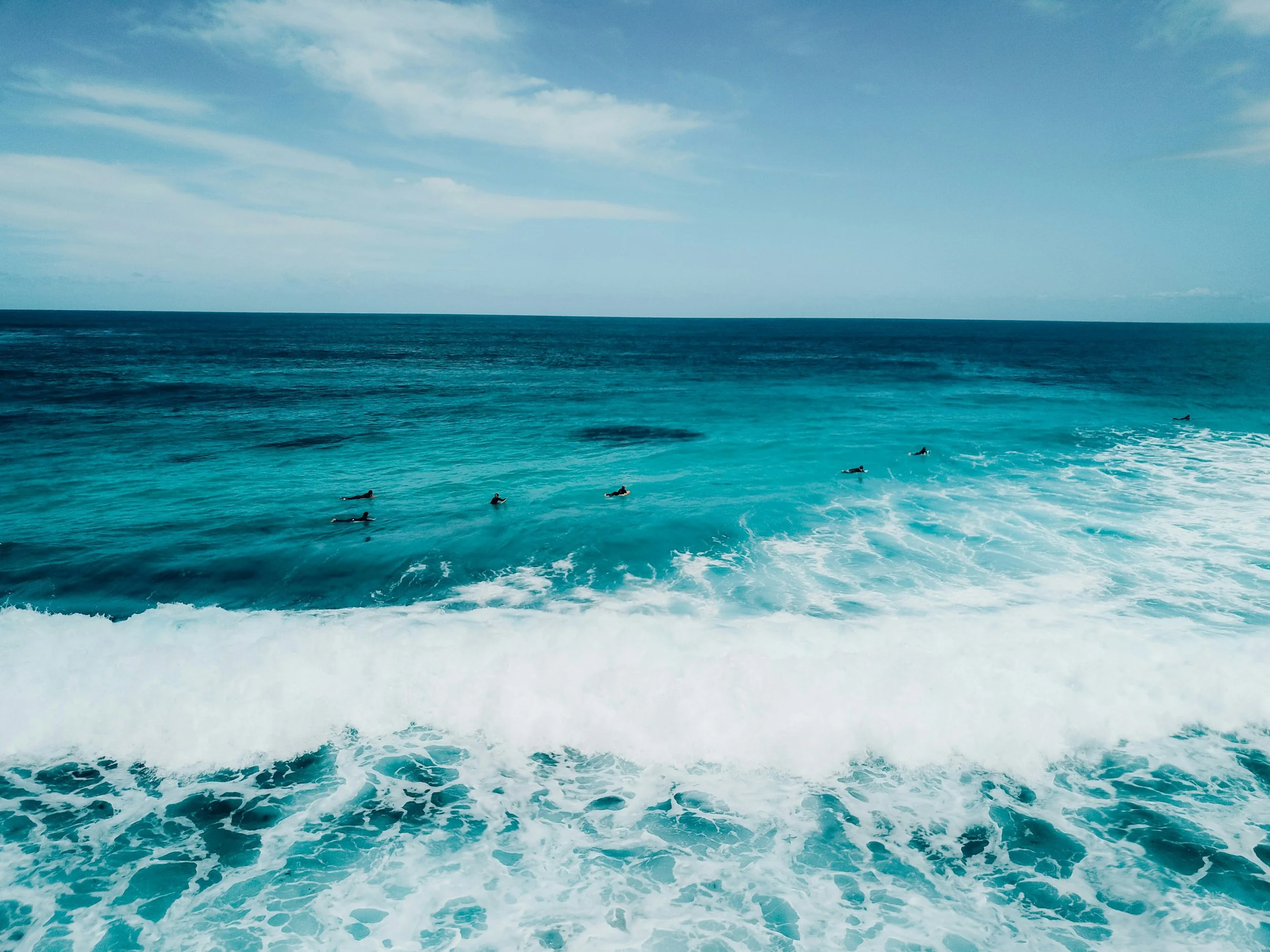 Surfers riding ocean waves under a blue sky with few clouds.