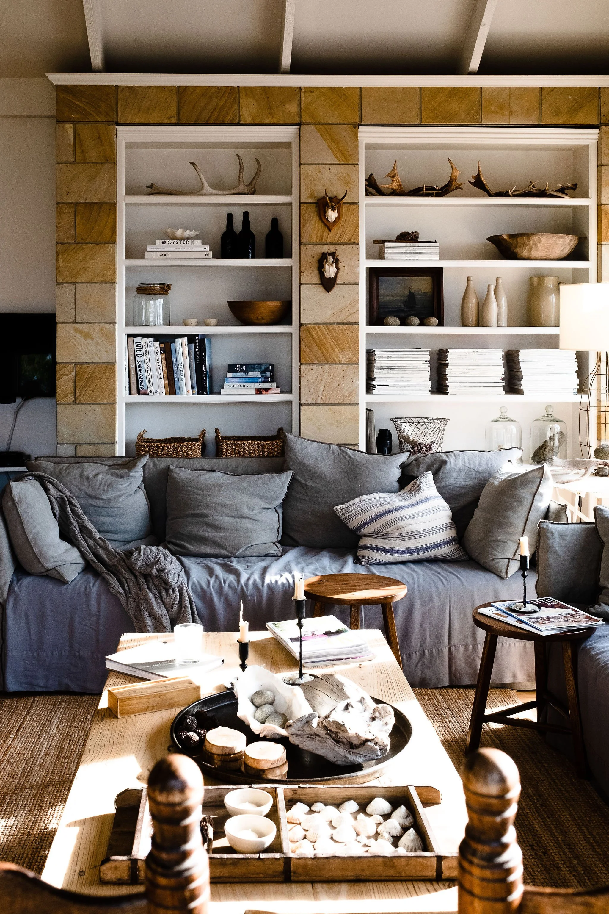 Cozy living room with gray sofa, wooden coffee table, built-in bookshelf with decorative items, candles, and a lamp.