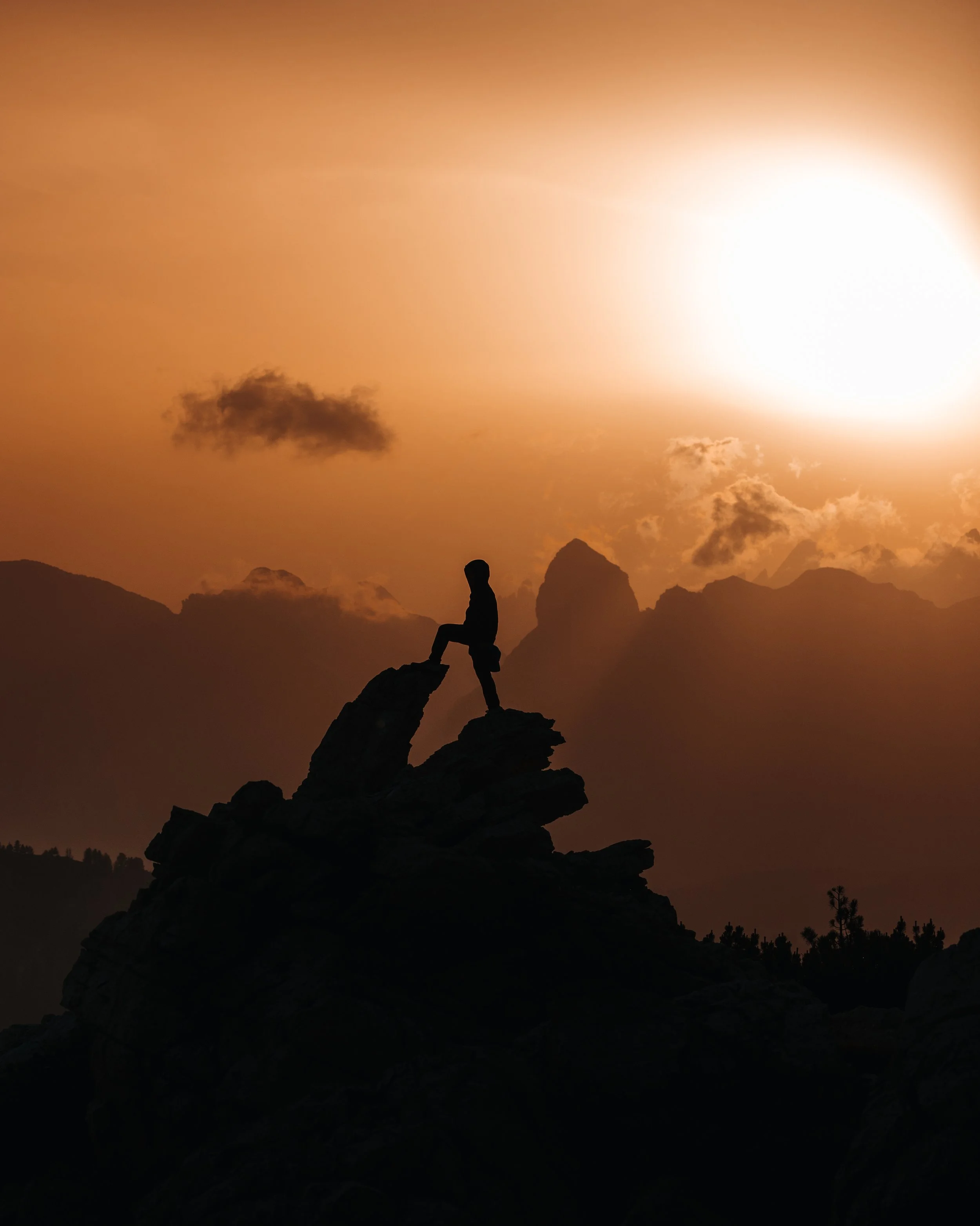 Person sitting on a rock formation at sunset with mountains in the background.