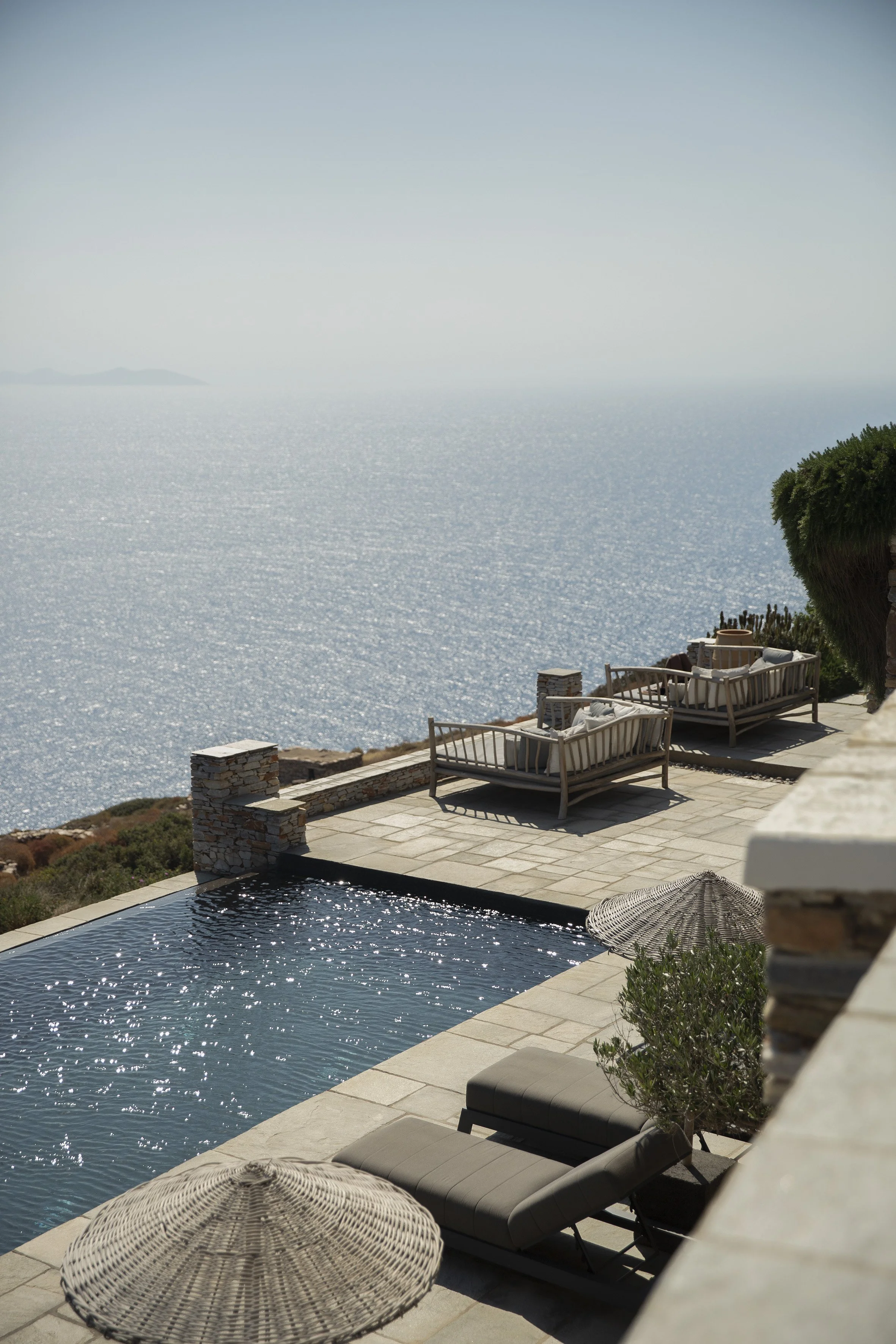 A luxurious outdoor pool area overlooking the ocean with loungers, umbrellas, and a scenic view.