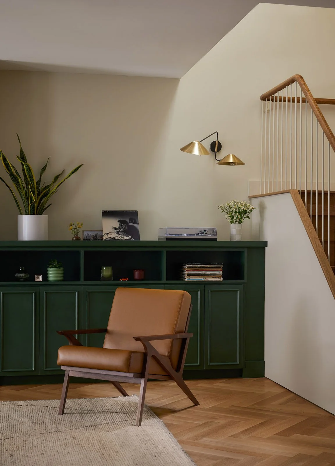Stair landing with green cabinetry, brass wall lights and a caramel leather lounge chair in a modern brownstone interior