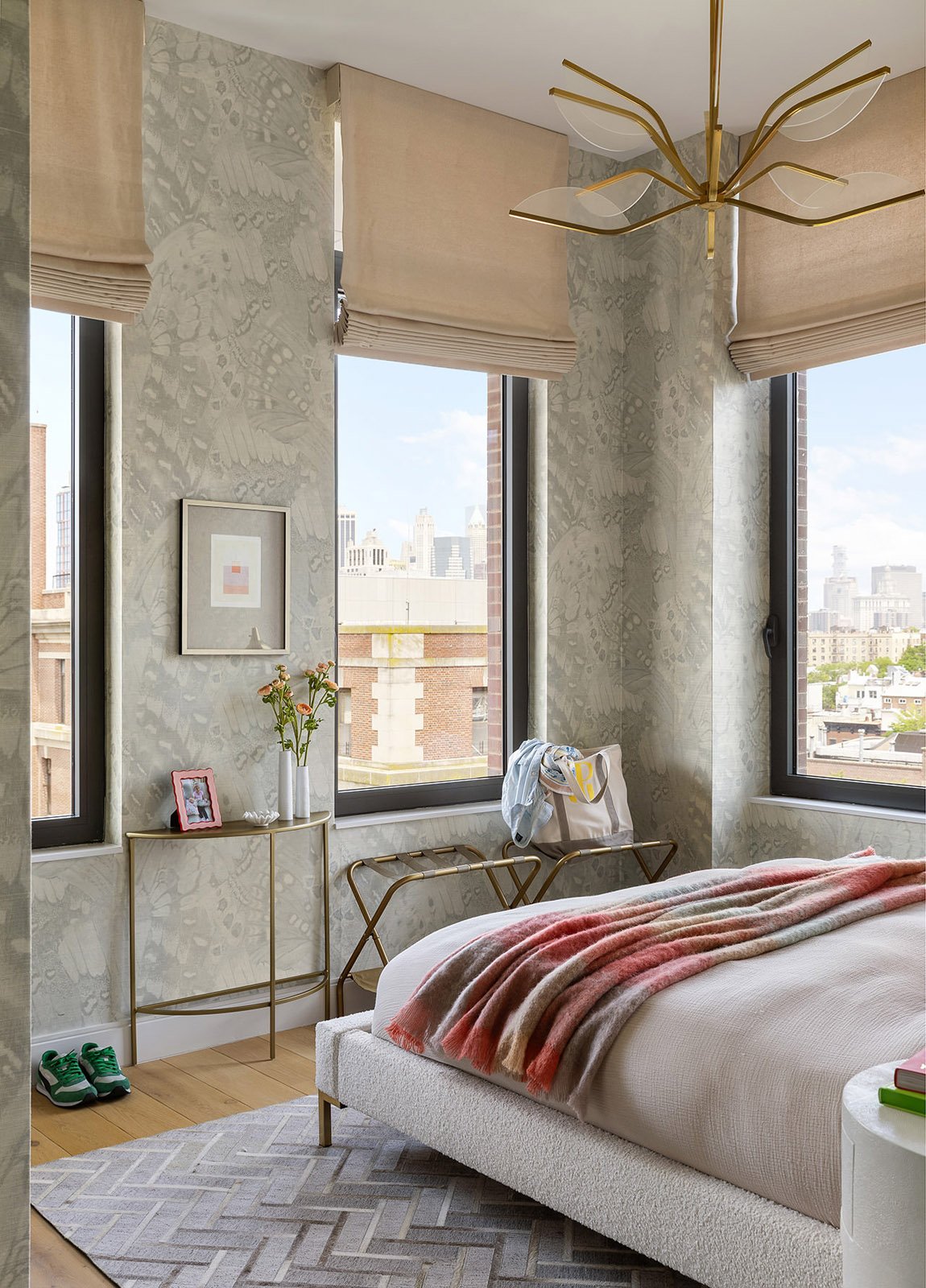 Bright bedroom corner with large windows, soft patterned walls and a cozy bed layered with warm textiles