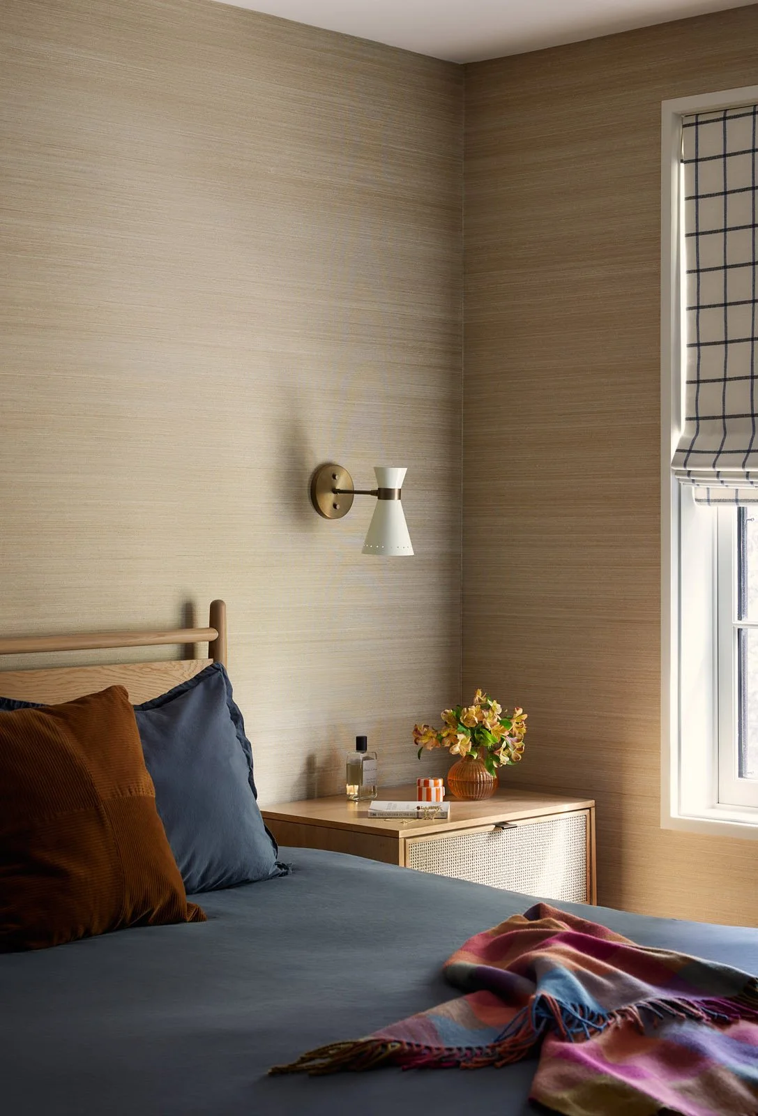 Modern bedroom with grasscloth wallpaper, brass sconce and simple nightstand styling for a calm, modern retreat