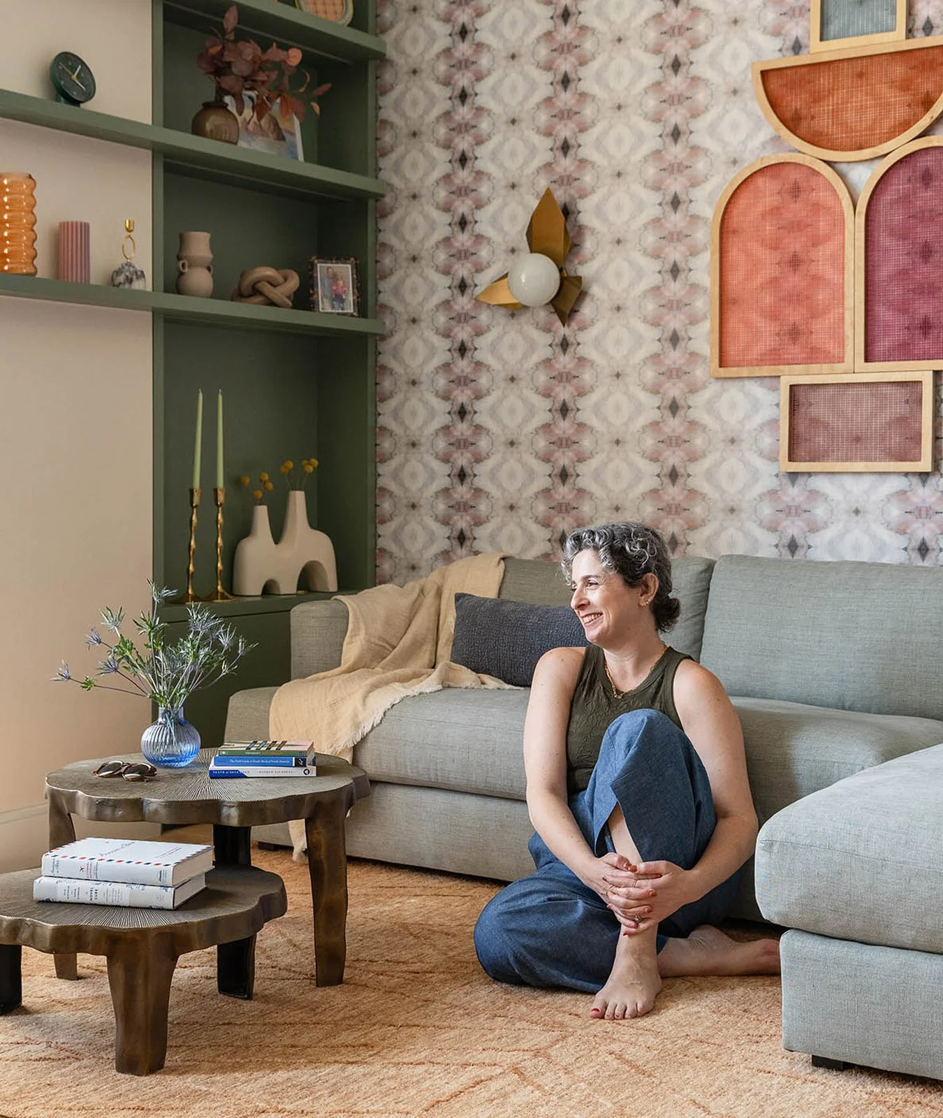 Interior designer Isabella Patrick smiling in the living room with patterned wall, sculptural art and rustic wood tables styled with books and flowers