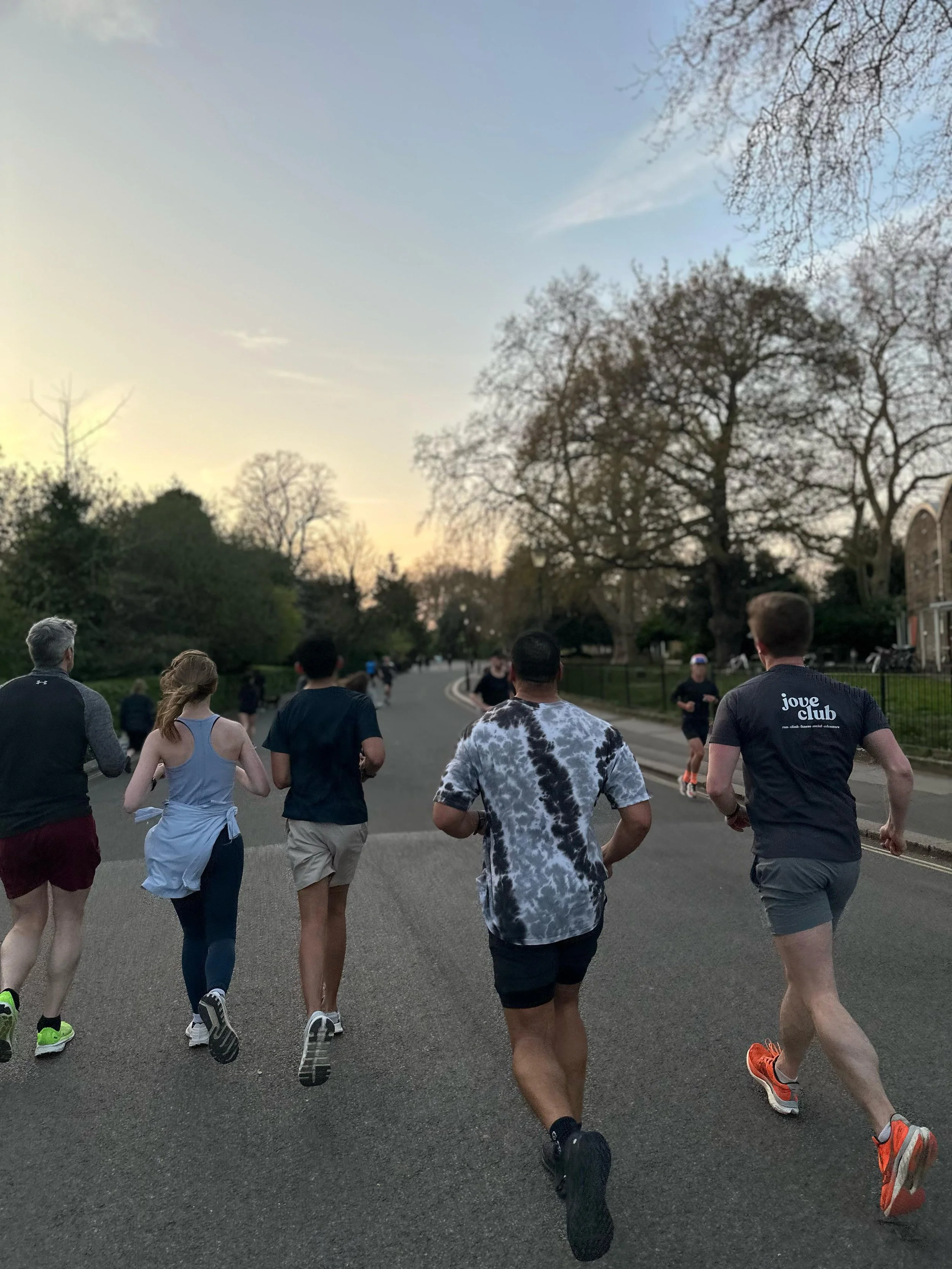 Group of people running on a paved street during sunset, with trees and residential houses on either side.