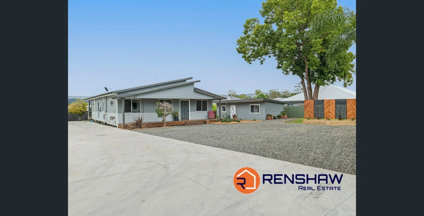 Exterior view of a modern, single-story house with a large gravel driveway and a landscaped yard. The house is painted light gray, has a metal roof, and features a small porch with potted plants. There is a tree and decorative fencing in the yard. The logo of Renshaw Real Estate is visible in the bottom right corner.