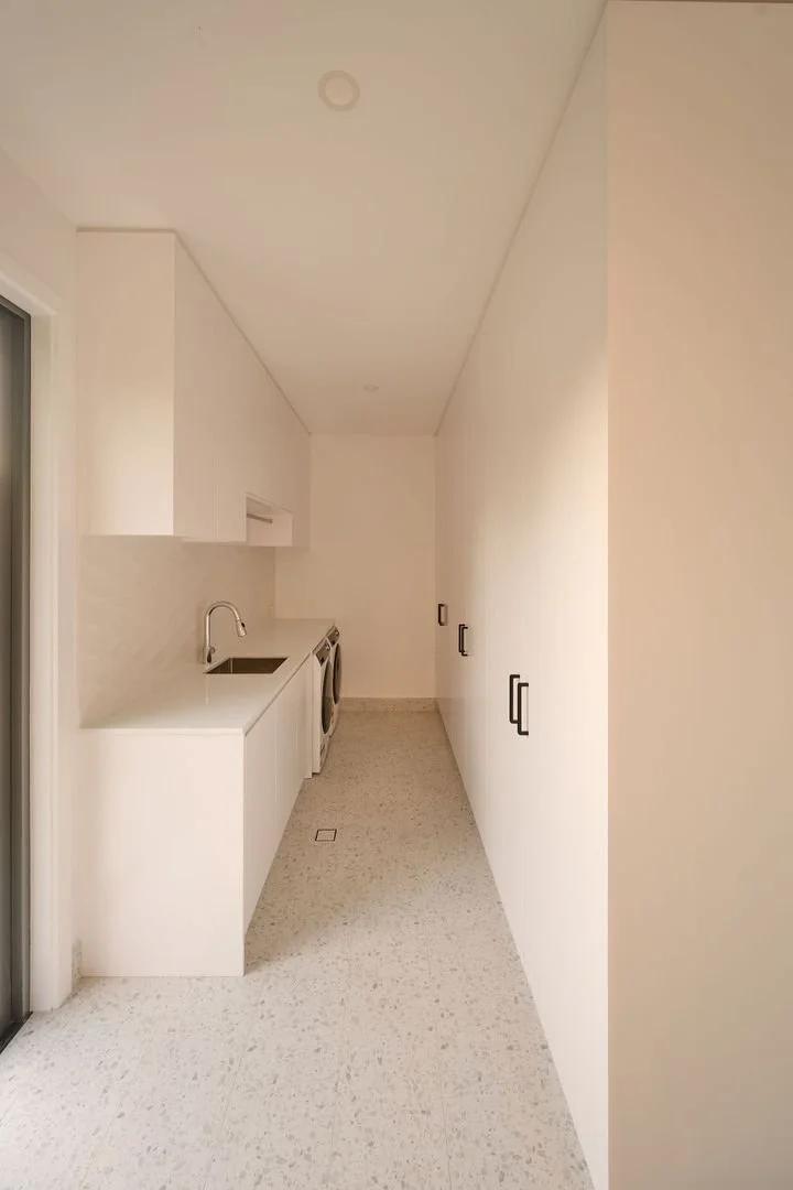 A laundry room with white cabinets, a countertop with a sink, a washing machine, and floor-to-ceiling storage cabinets, all in a minimalist design.