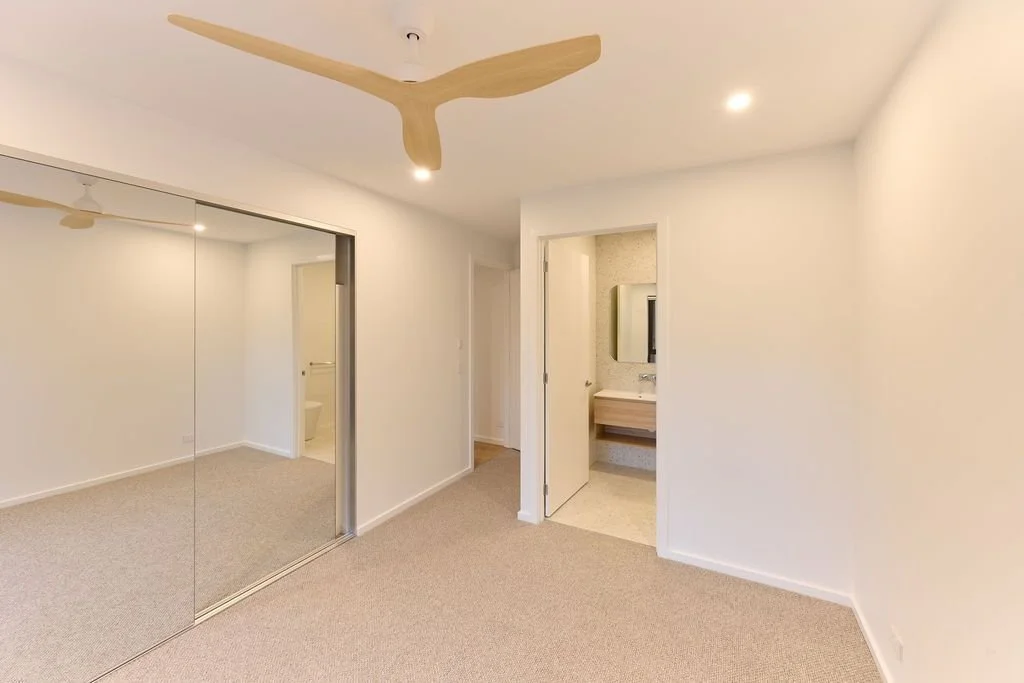 Empty bedroom with a ceiling fan, large mirrored closet doors, and a small bathroom with a sink and mirror.