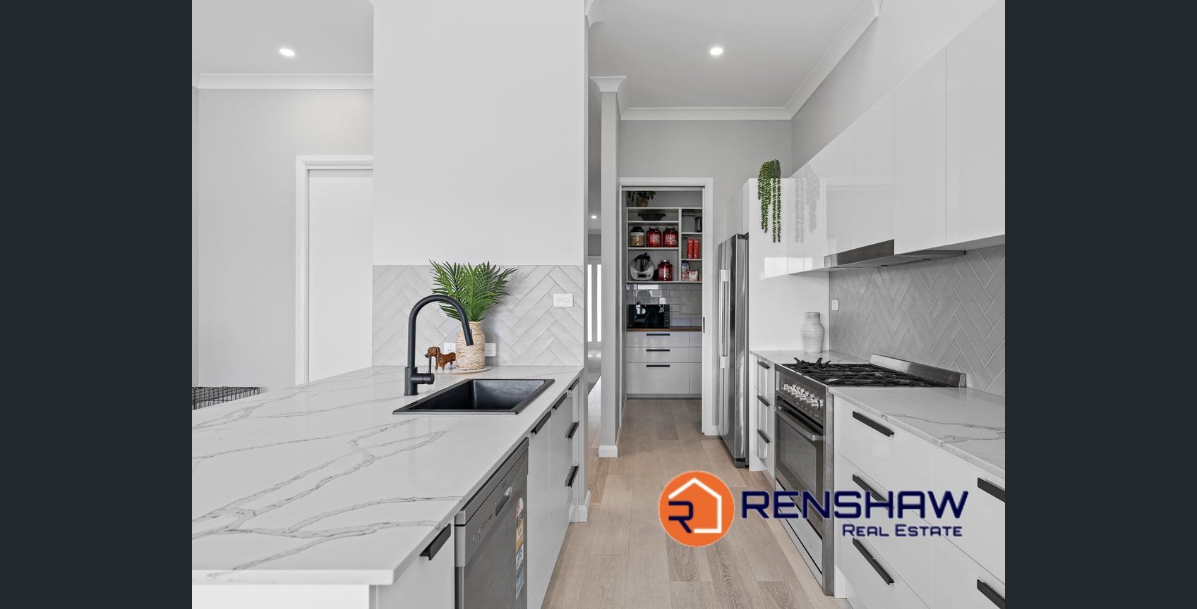 Modern white kitchen with marble countertops, black sink, black faucet, stainless steel appliances, wooden flooring, and decorative plants. Renshaw Real Estate logo is in the bottom right corner.