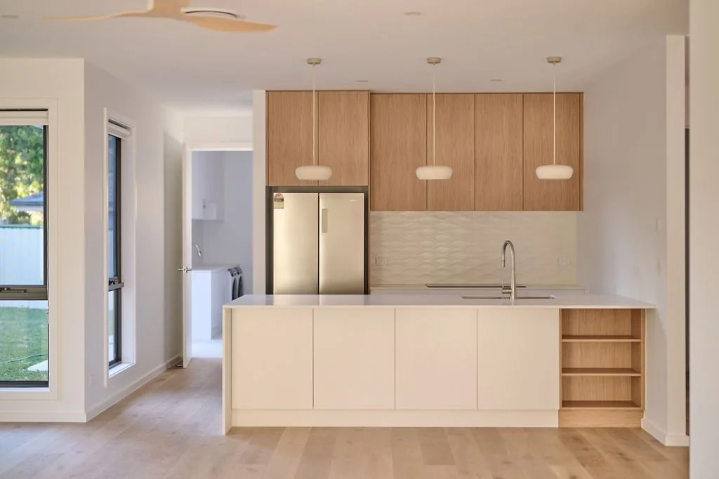 Modern kitchen with white island, light wood cabinets, a double-door refrigerator, and three hanging pendant lights.