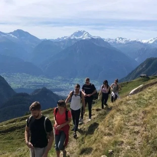 Gruppe von fünf Menschen wandert in den Bergen mit schneebedeckten Gipfeln im Hintergrund.