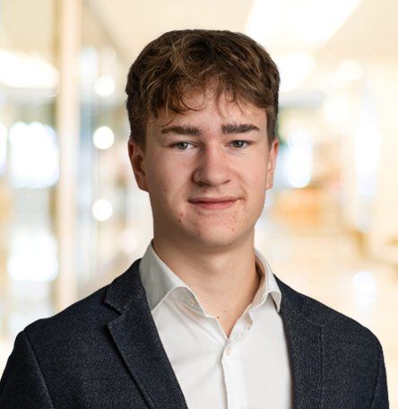 Ein junger Mann in einem weißen Hemd und dunklem Blazer vor hellem Hintergrund.