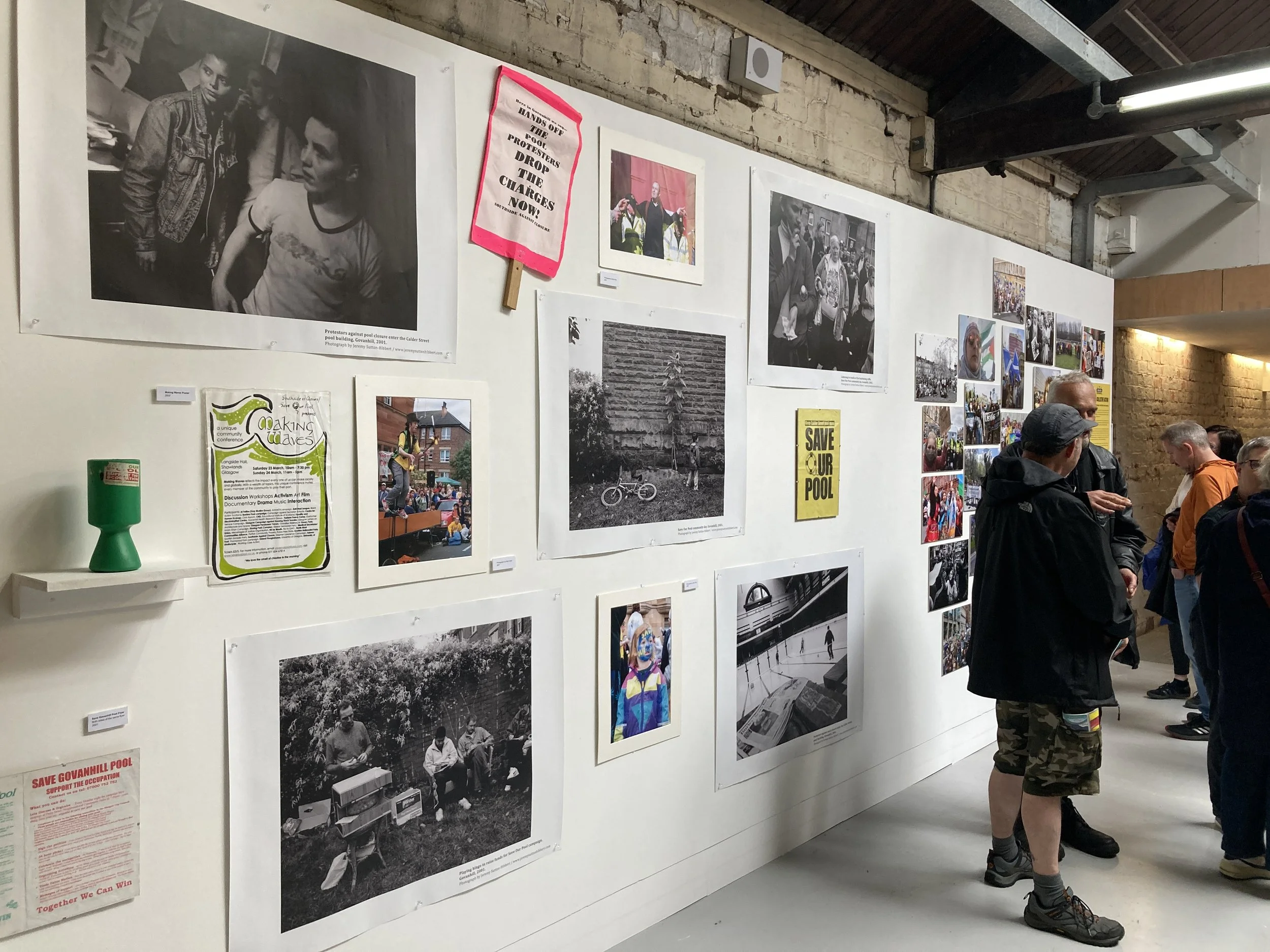 Colour photograph showing people to right of image socialisng at a photography exhibition. Black and white large photos are on the wall.