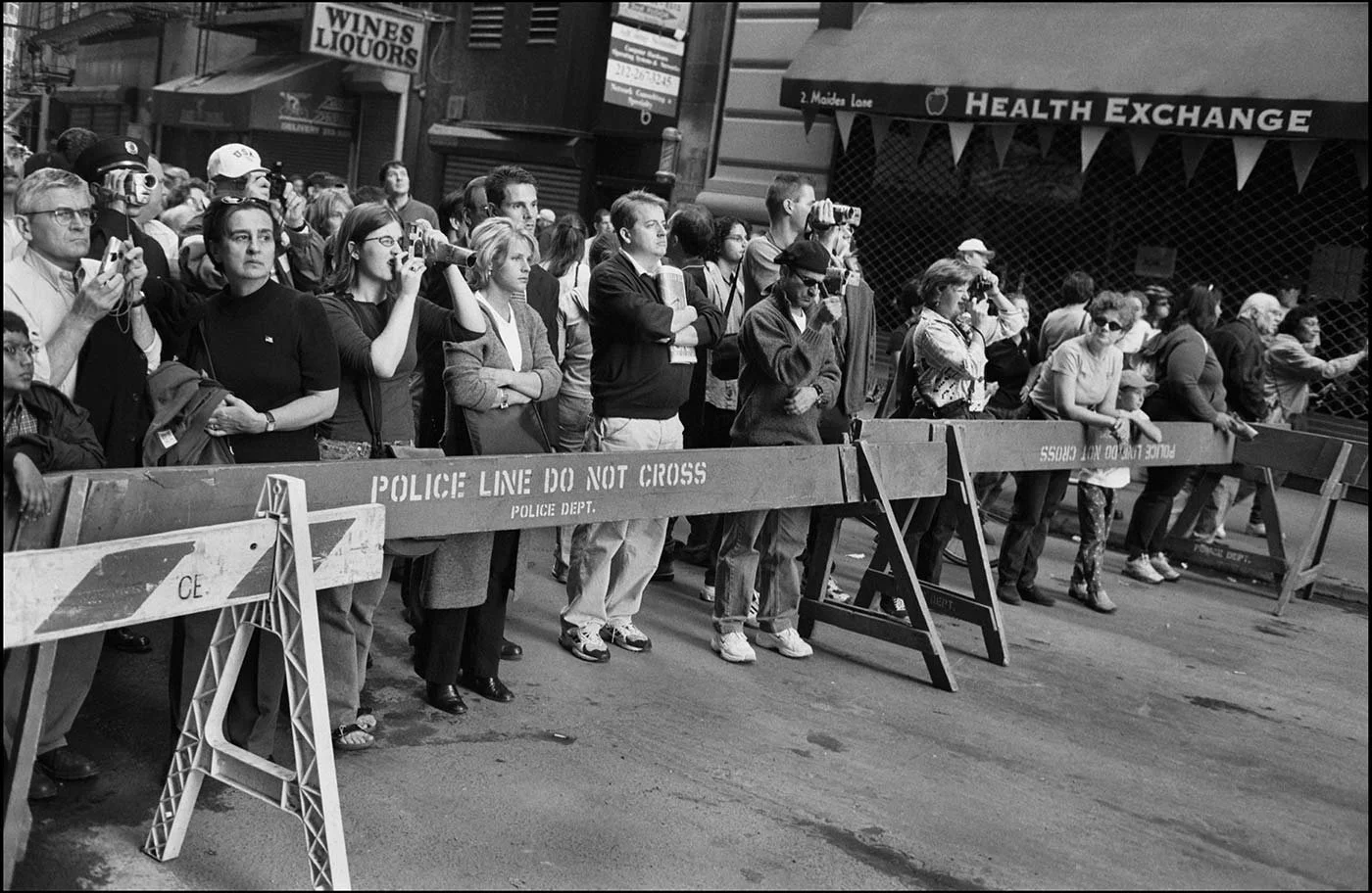 Black and white photo of spectators standing behind a barrier which reads Police Line Do Not Cross.