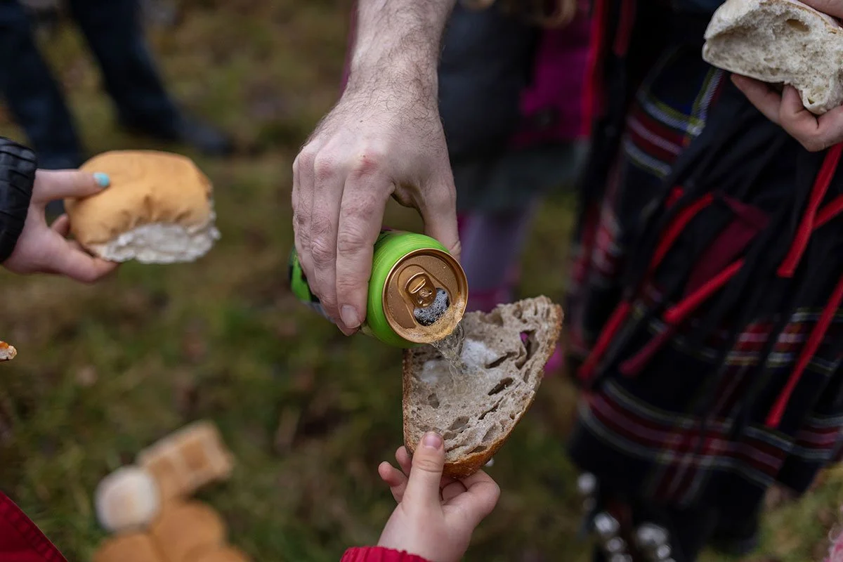 A hand purs cider from a green can onto a piece of bread held out by a young child's hand.