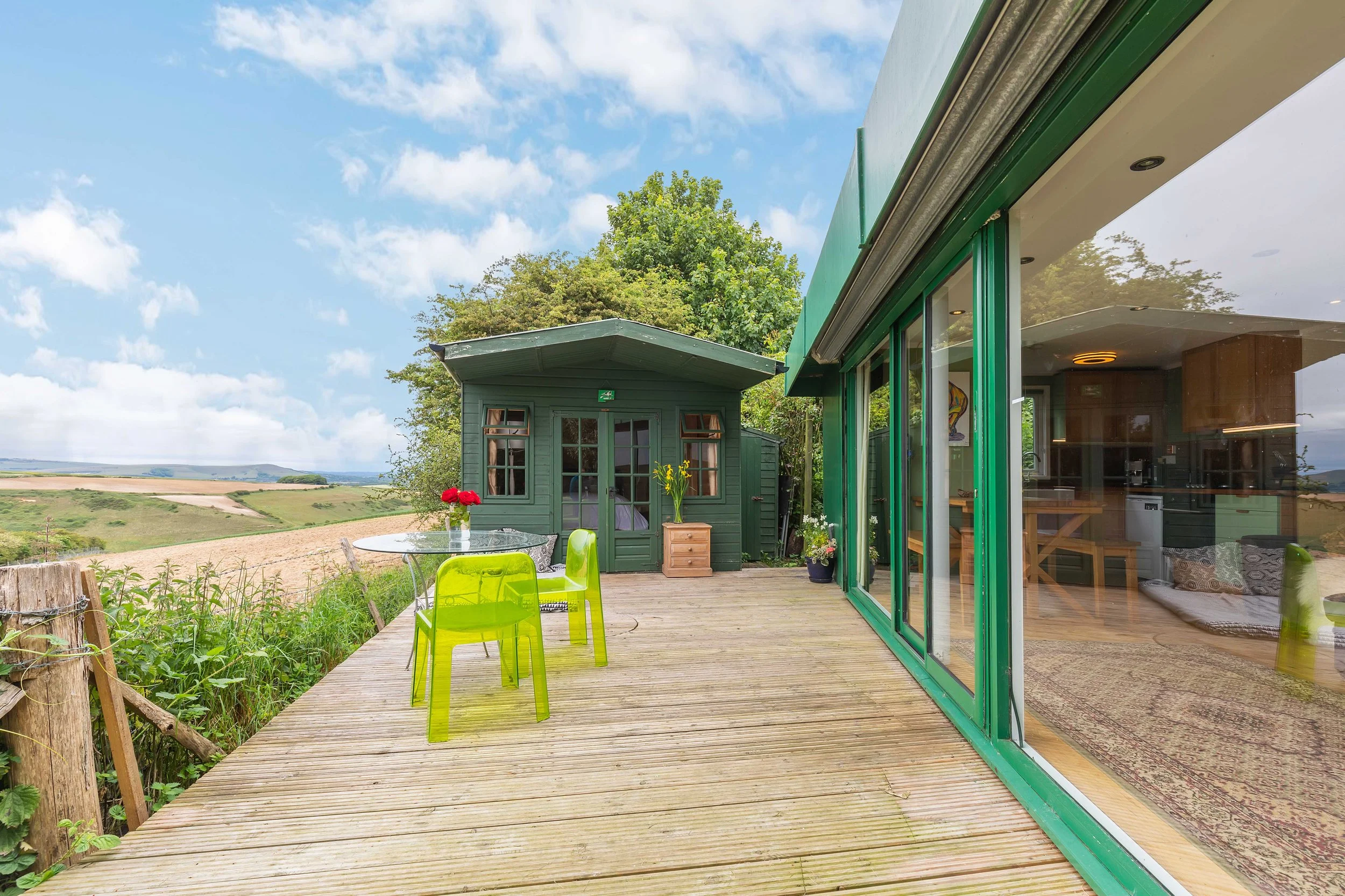Wooden deck with green chairs overlooking serene fields, a peaceful retreat for unwinding after creative sessions