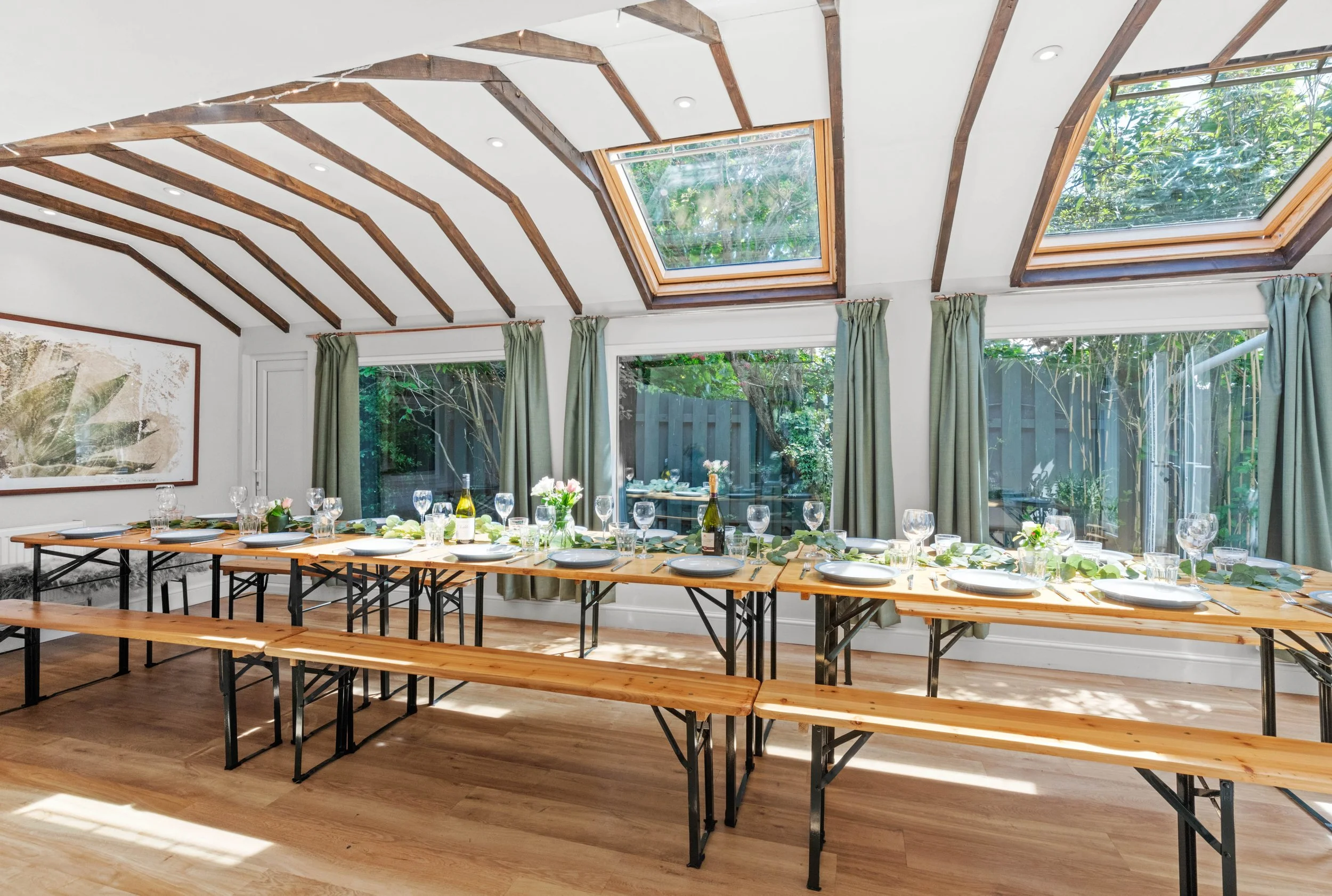 A bright and airy dining hall with long wooden tables, skylights, and elegant table settings, ideal for group dining during retreats.