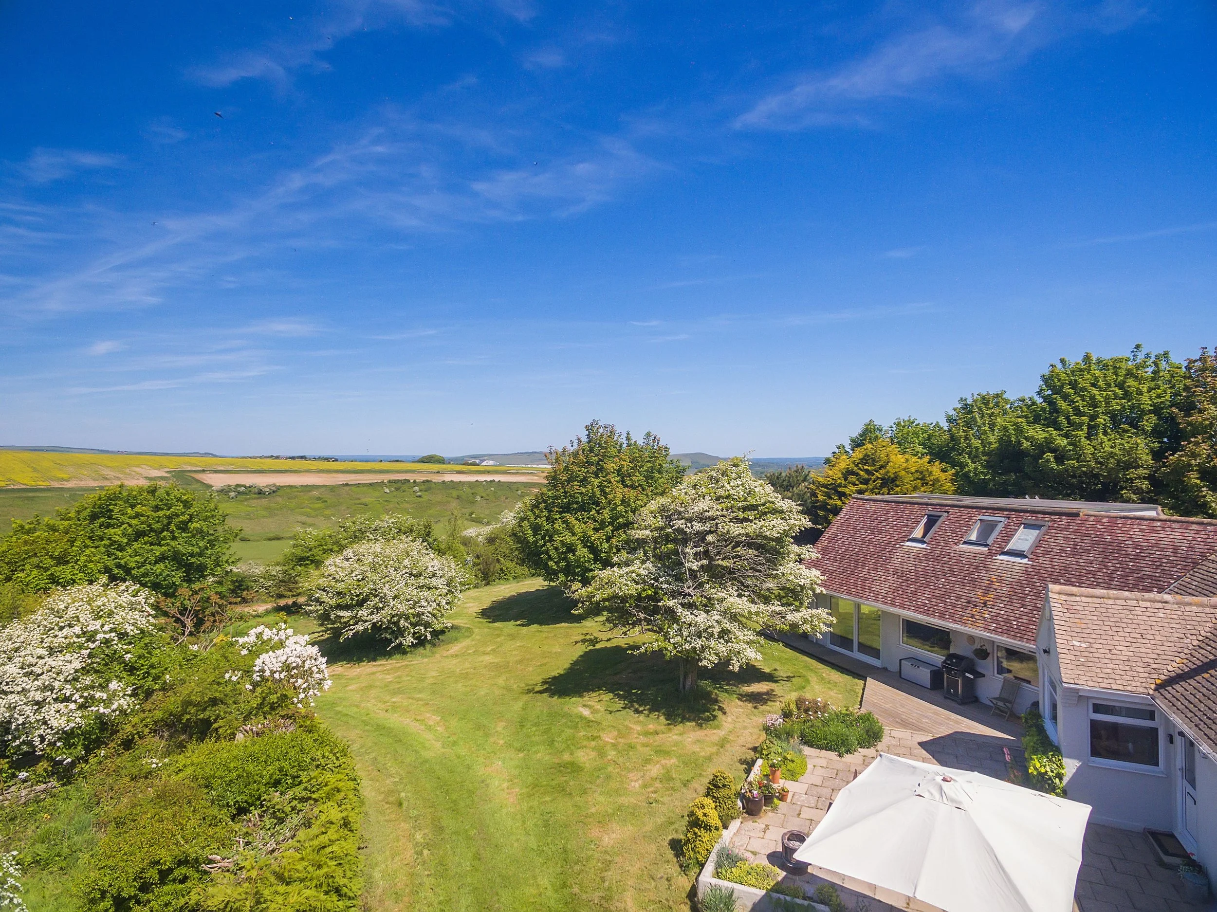 Aerial view of a UK retreat accommodation, surrounded by sprawling green fields, trees, and vibrant blue skies, ideal for peaceful retreats in the countryside