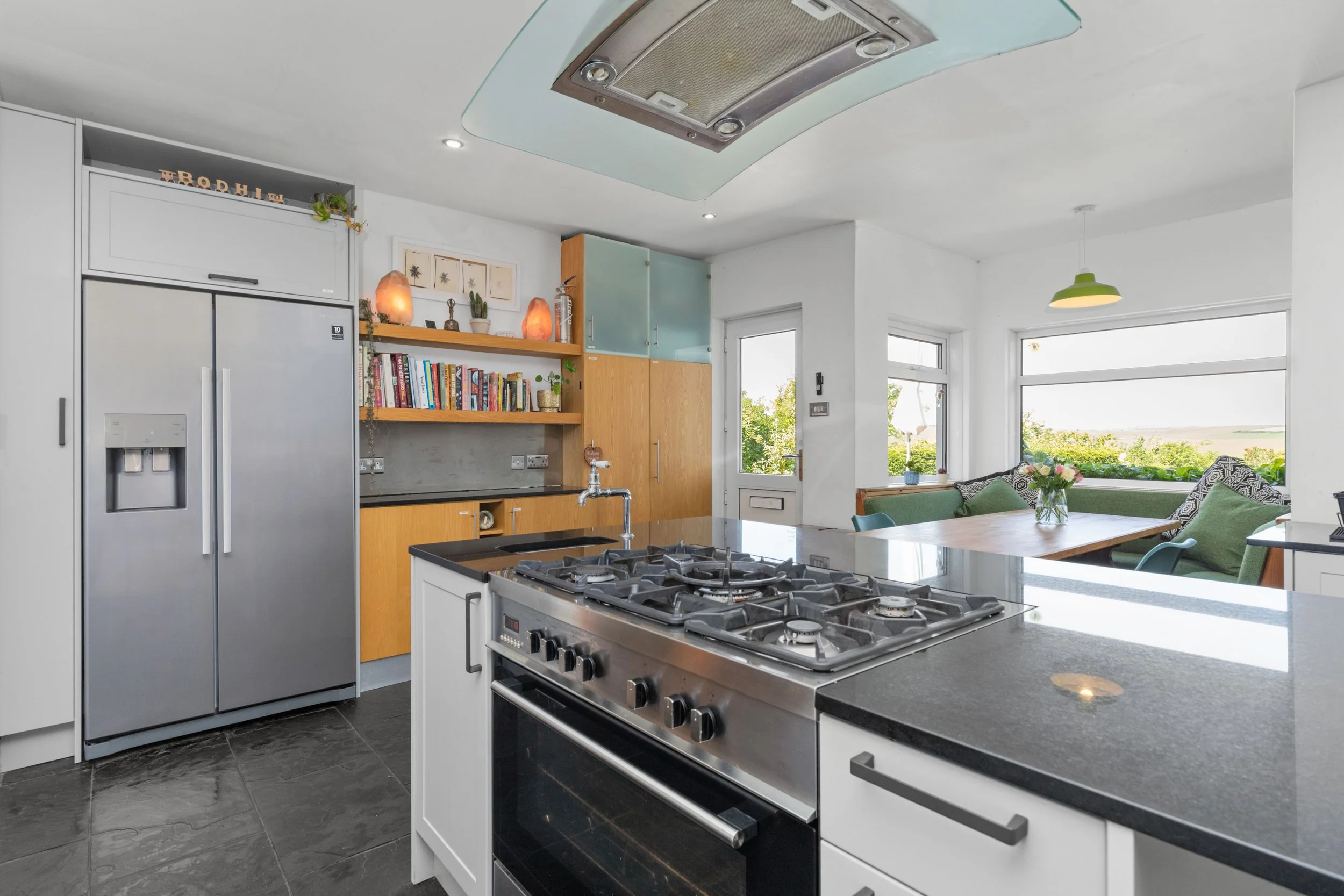 A spacious modern kitchen with a central island, gas stove, and cozy dining nook with countryside views, perfect for preparing group meals during retreats.