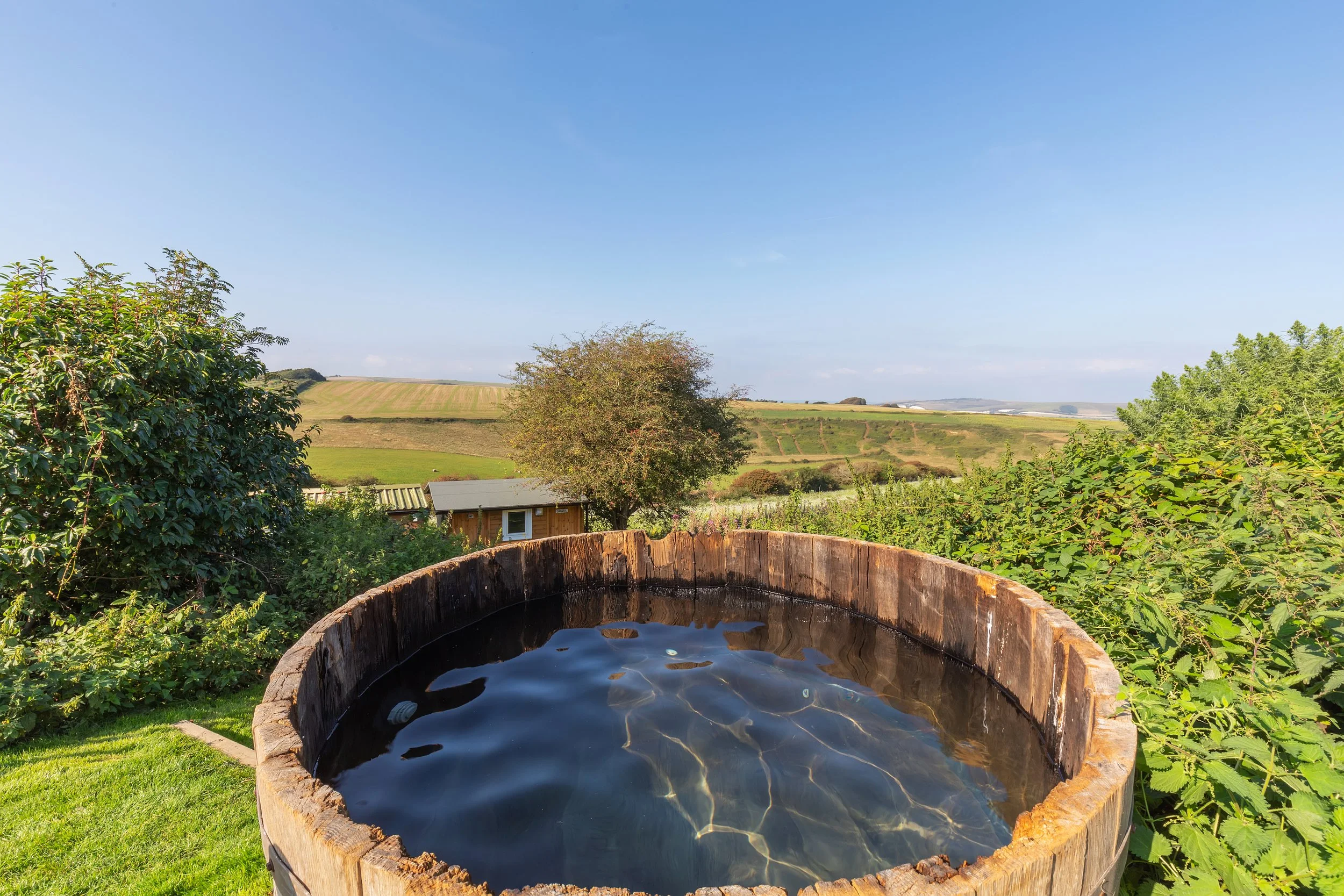 Rustic wooden hot tub in the garden of a UK retreat accommodation, surrounded by natural greenery and overlooking picturesque fields, perfect for relaxation during UK retreats