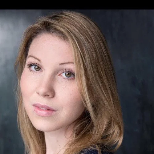 Portrait of a young woman with blonde hair and light makeup against a dark background.