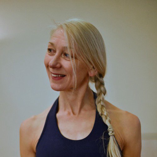 A woman with long blonde hair in a braid, smiling and wearing a navy tank top.