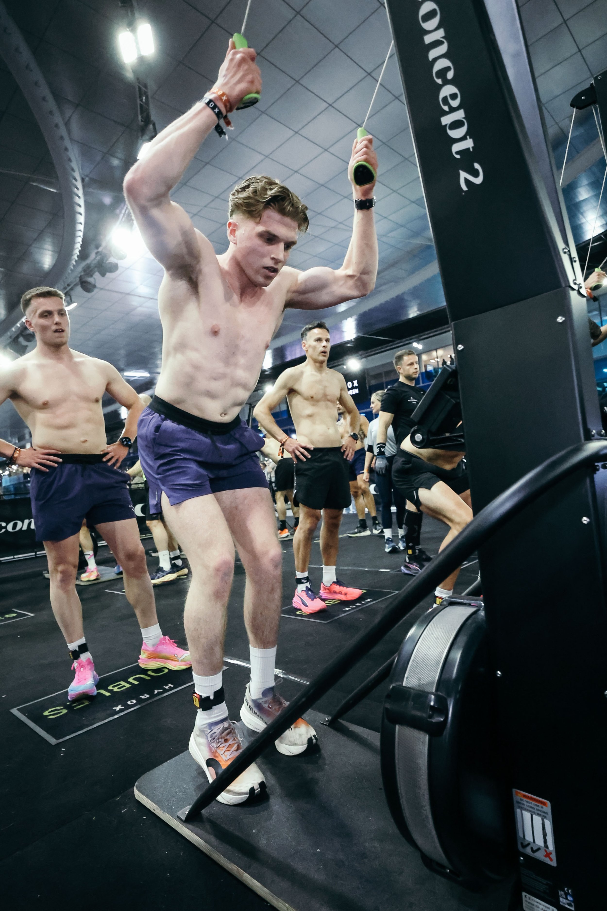 Man op een loopband in een sportschool die zich voorbereidt op een hardlooptraining, omringd door andere sporters.
