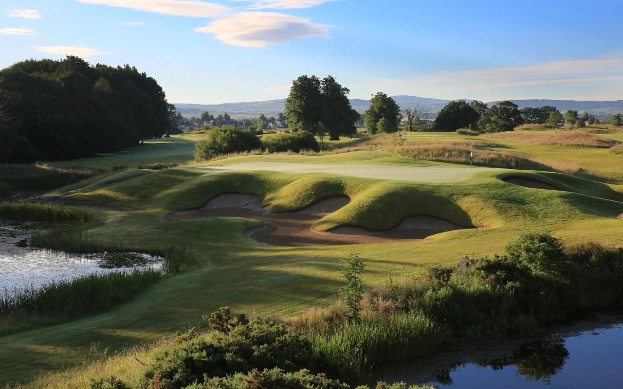 A scenic golf course with sand traps, green fairways, and trees, under a blue sky with some clouds.