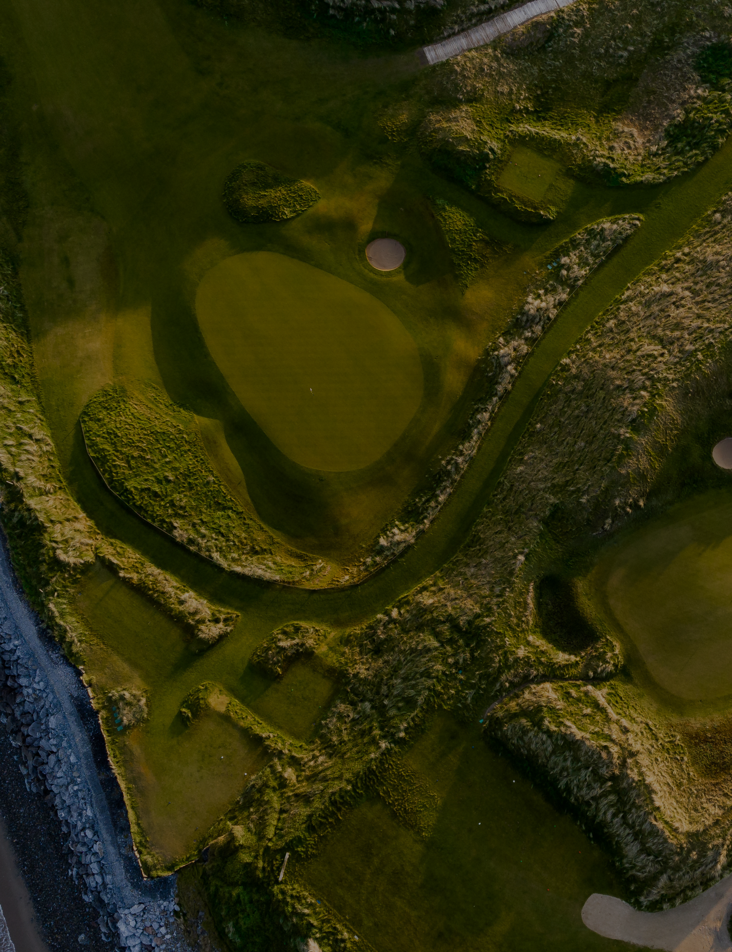 Aerial view of a golf course with green grass, sand bunkers, and surrounding trees and hills.