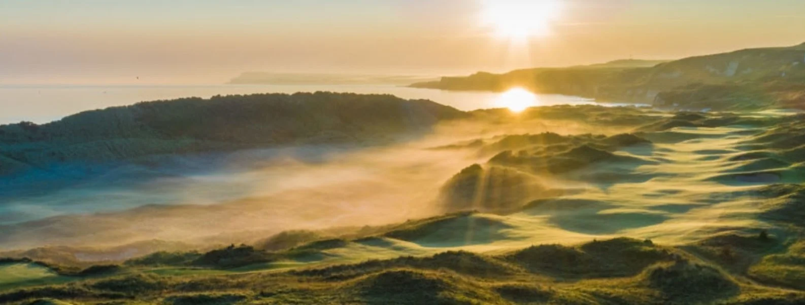 Royal Portrush Golf Links at sunrise, golden light over the fairways and dunes along Northern Ireland's Causeway Coast