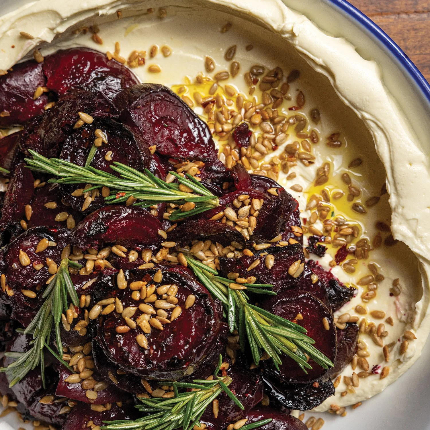 A close-up view of a dish featuring roasted beet slices topped with sunflower seeds and sprigs of fresh rosemary, surrounded by whipped ricotta.