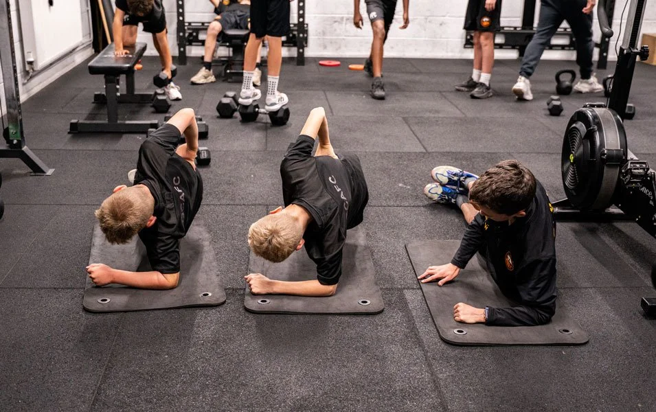 Three young athletes stretch on yoga mats in gym