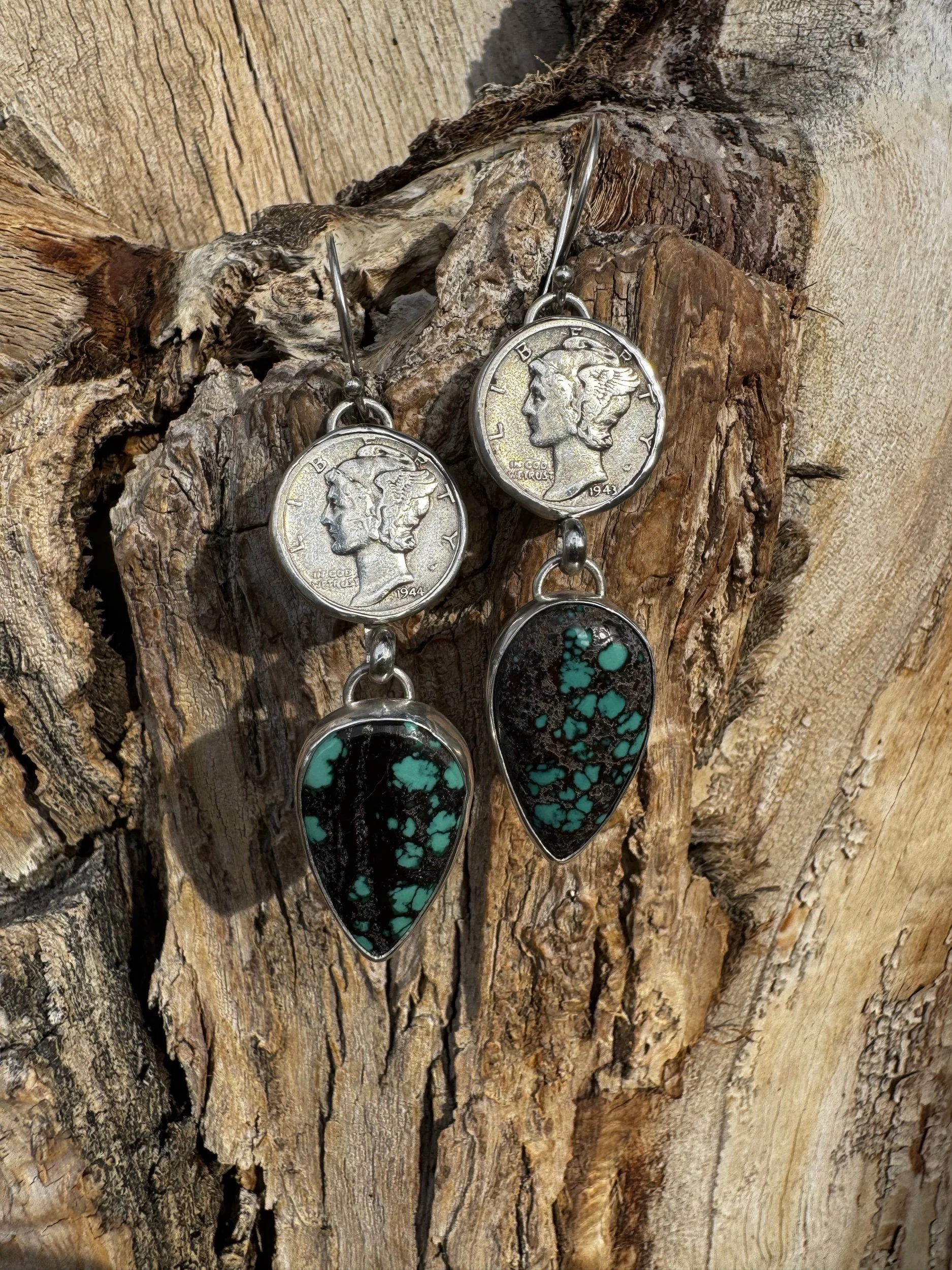 Pair of earrings with dime coins and teardrop-shaped turquoise stones hanging below, displayed on a textured wooden surface.