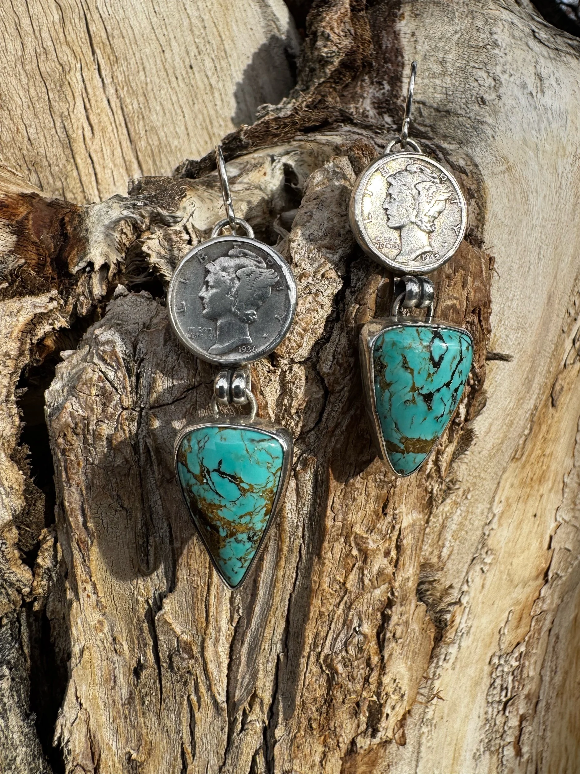 Pair of earrings with coin tops and large turquoise stone pendants hanging from a piece of driftwood.