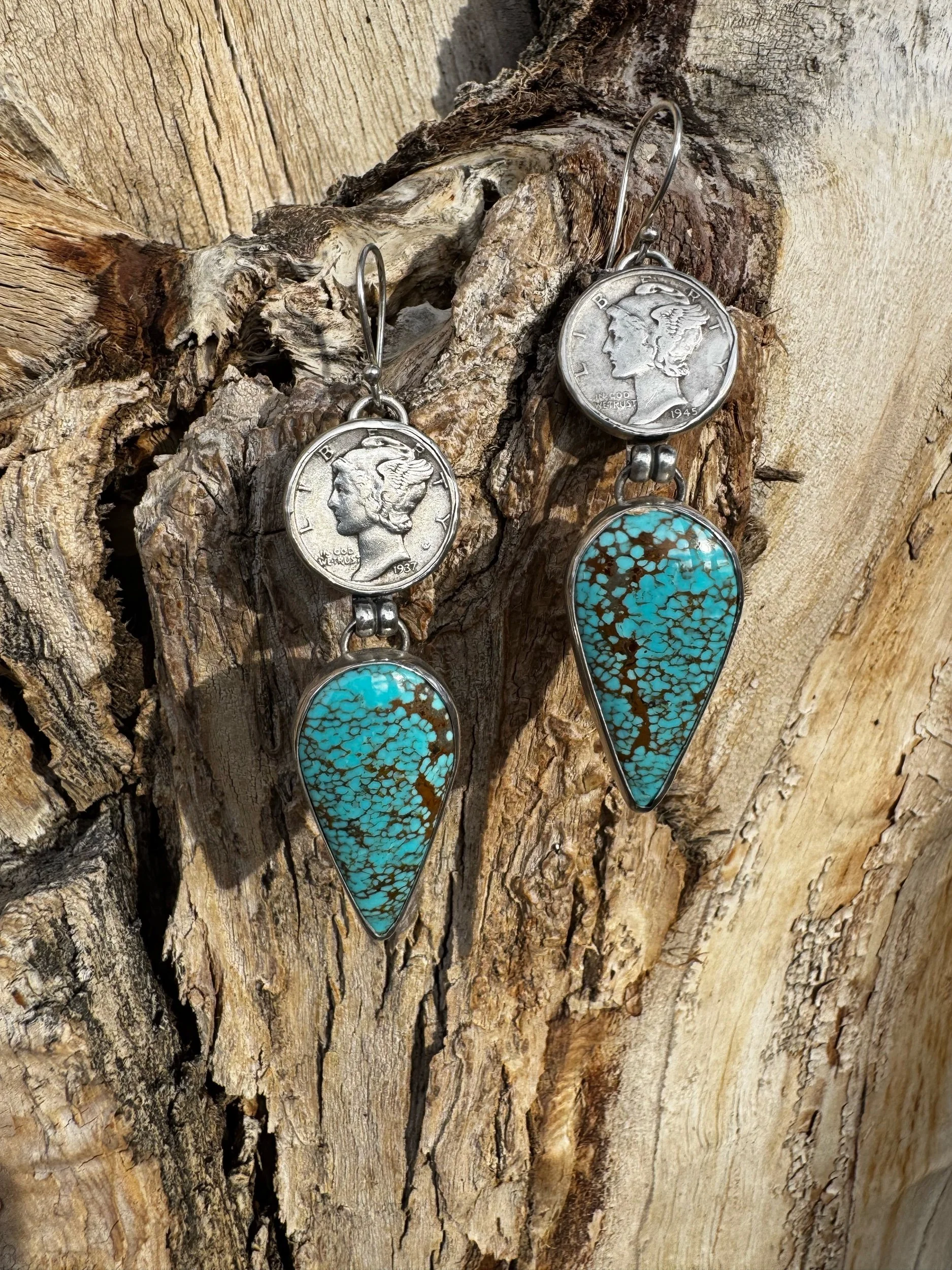 Earrings made from U.S. dimes with turquoise stone pendants hanging on a textured wood surface.