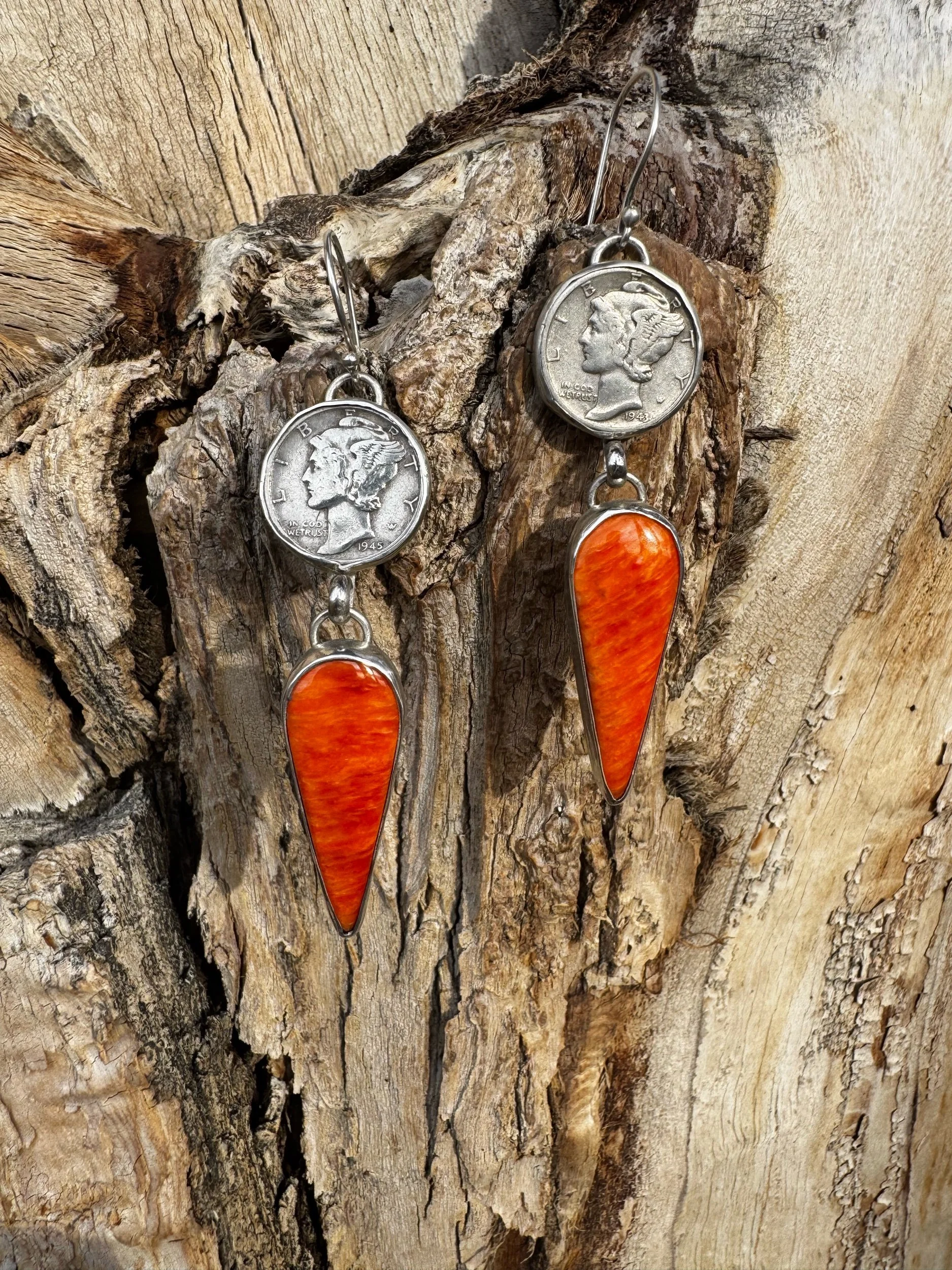 Earrings made with a U.S. 1945 quarter and orange teardrop-shaped stones hanging on a rustic wooden background.