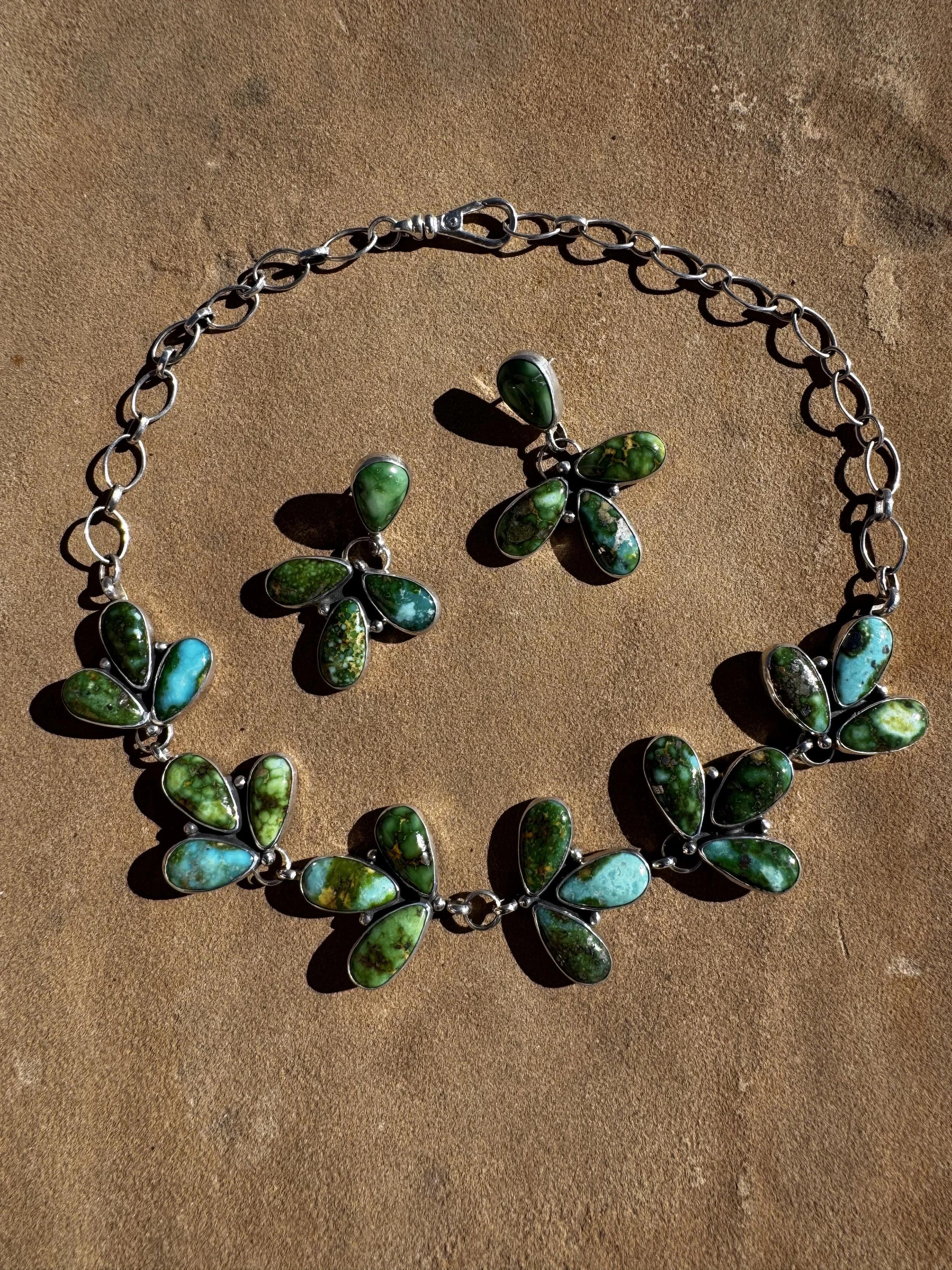 A jewelry set consisting of a necklace and earrings, featuring butterfly-shaped designs with green and blue marbled stones set in silver.