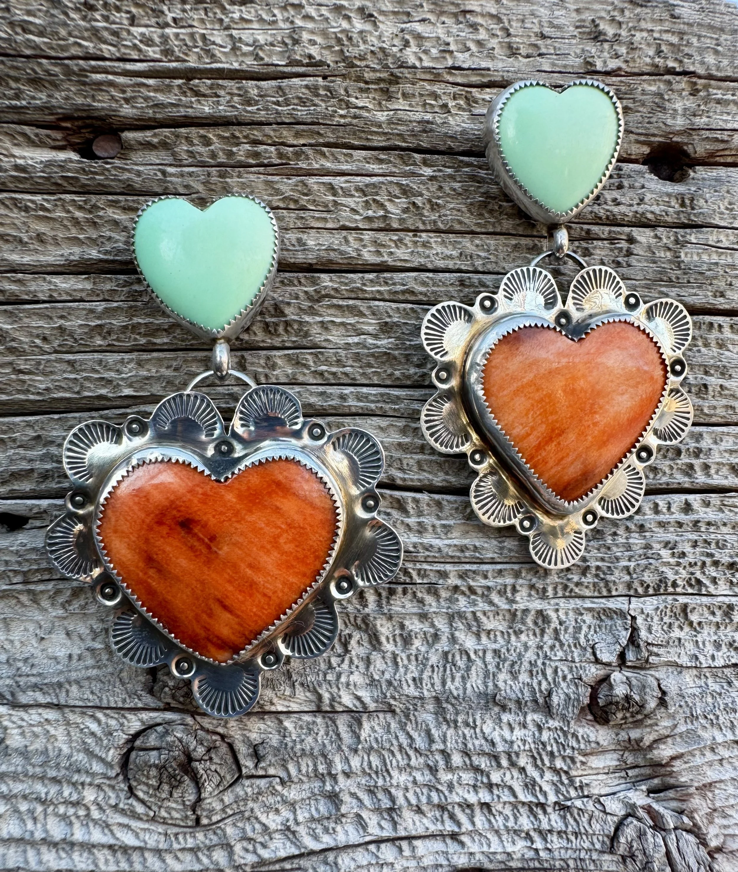 Pair of turquoise and coral heart-shaped earrings with silver detailing, placed on weathered wood surface.