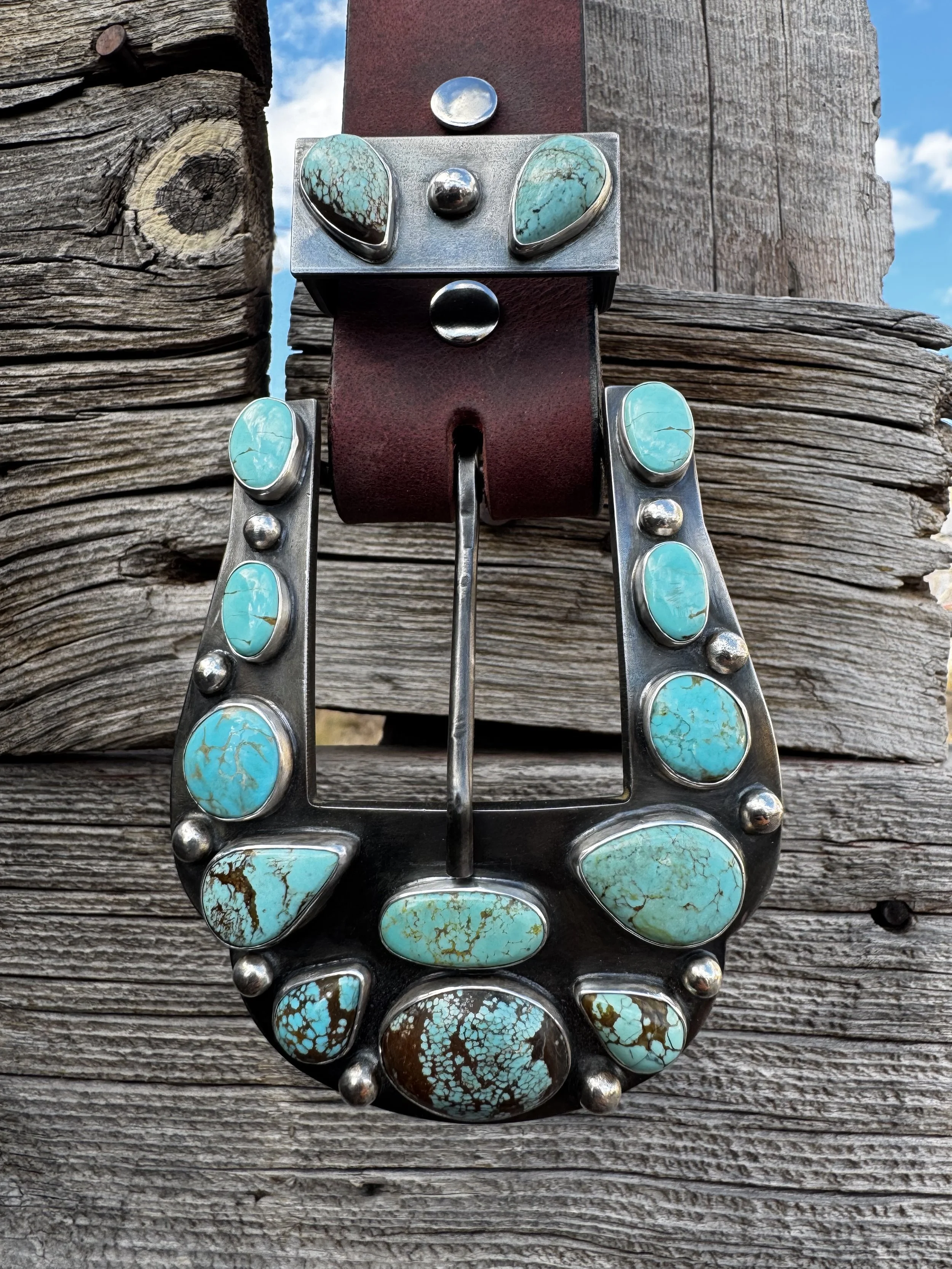 Close-up of a decorative belt buckle with turquoise stones mounted on a distressed wooden fence.