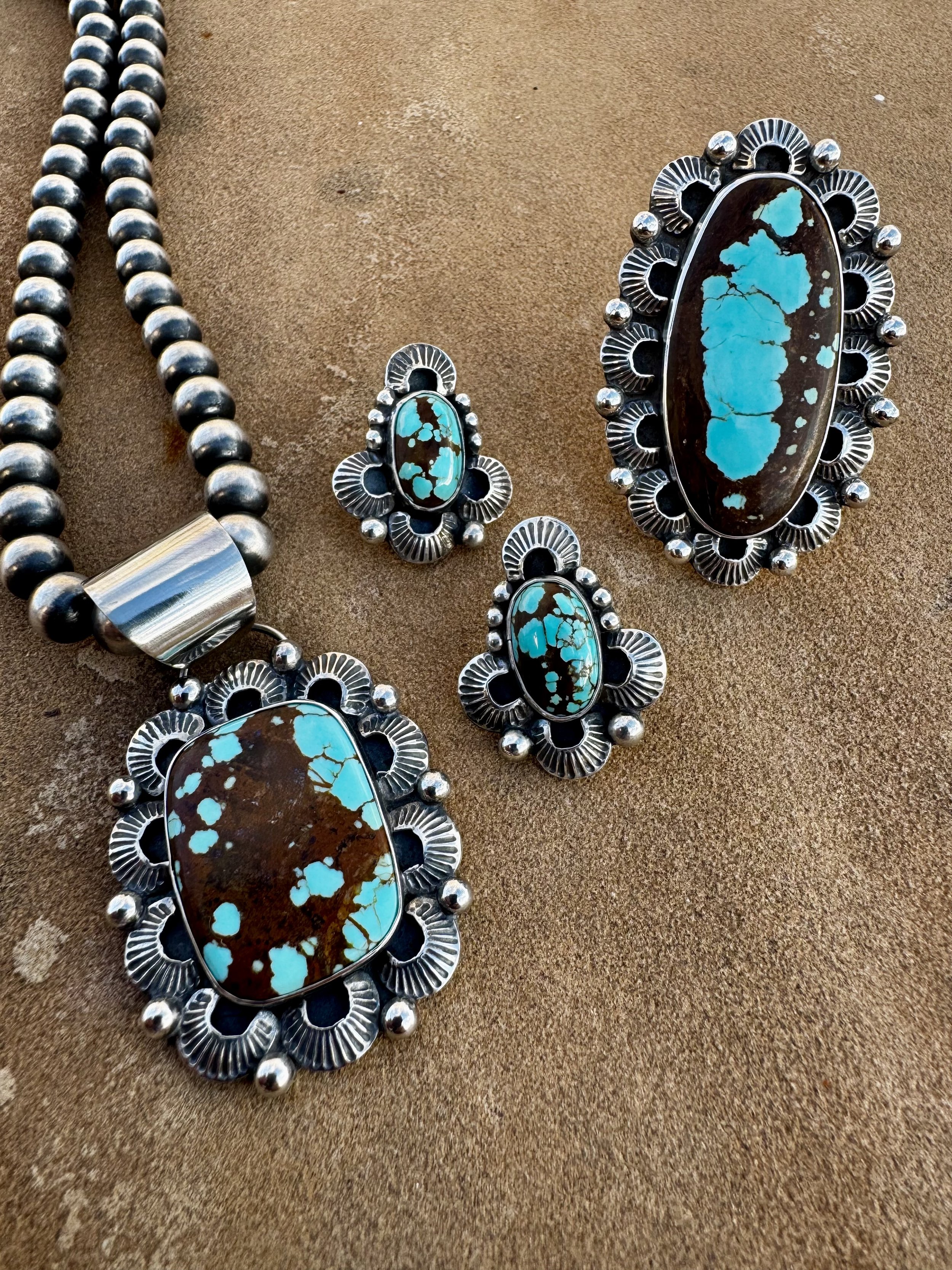 Set of turquoise and silver jewelry including a necklace and earrings on a brown surface.