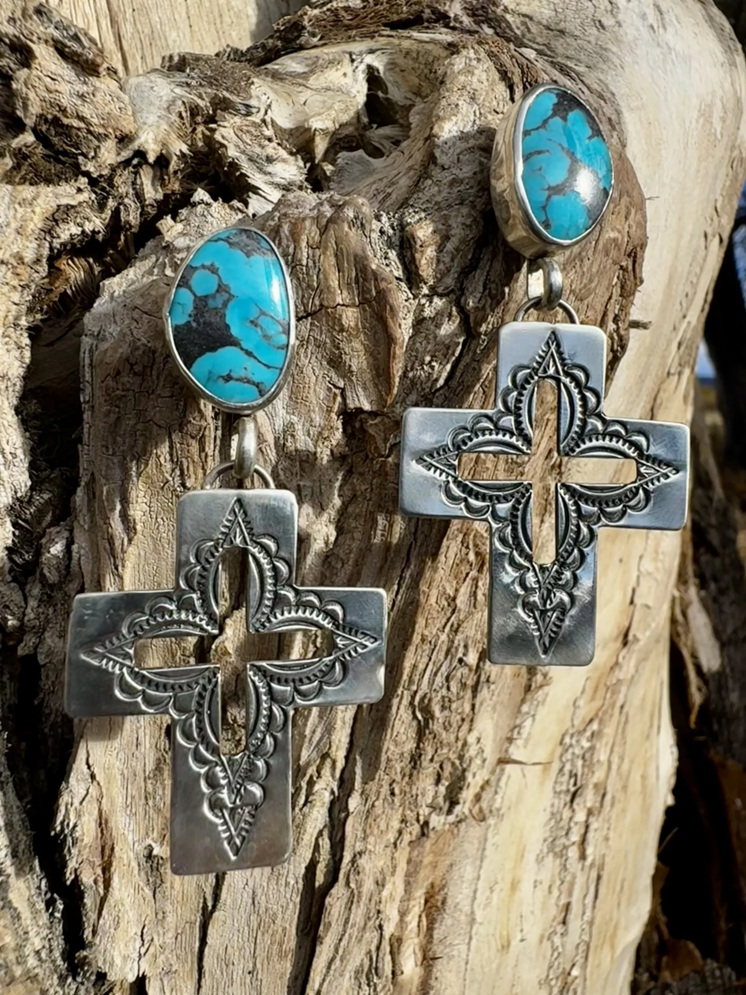 Pair of silver earrings with turquoise stones, hanging from weathered wood.
