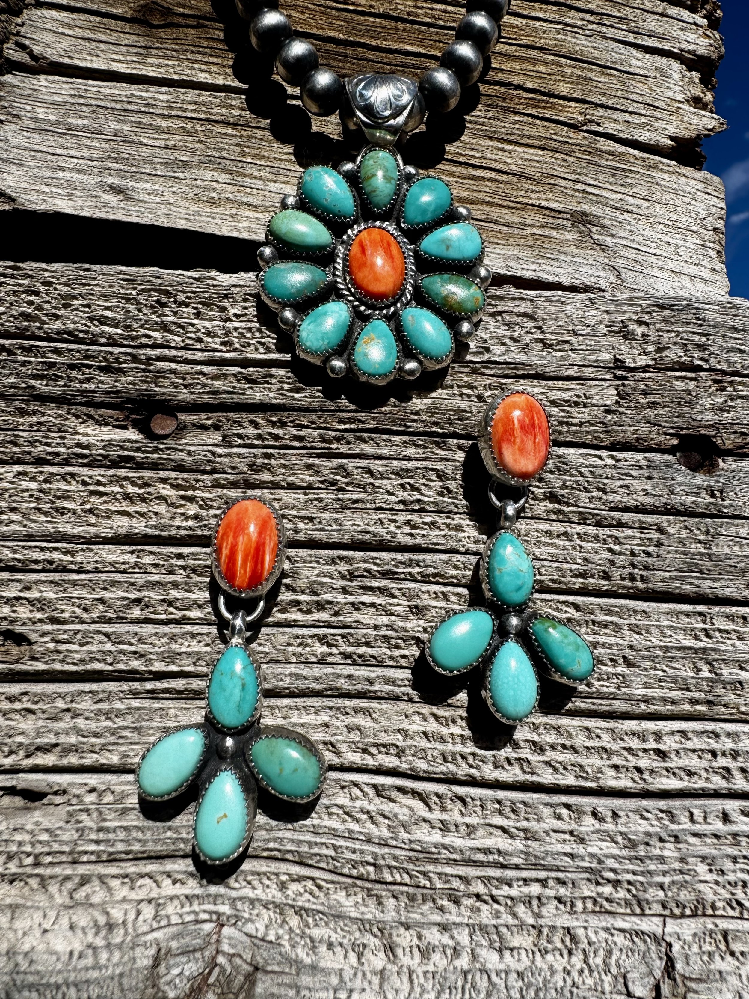 Turquoise and coral jewelry set including a necklace and earrings, displayed on weathered wooden surface.