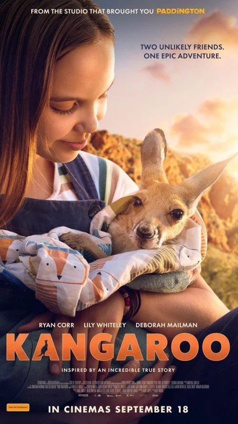 Poster for the movie "Kangaroo" featuring a girl holding a small dog in a blanket, with mountains and sunset in the background. Text includes "From the studio that brought you Paddington," "Two unlikely friends. One epic adventure," and "In cinemas September 18."