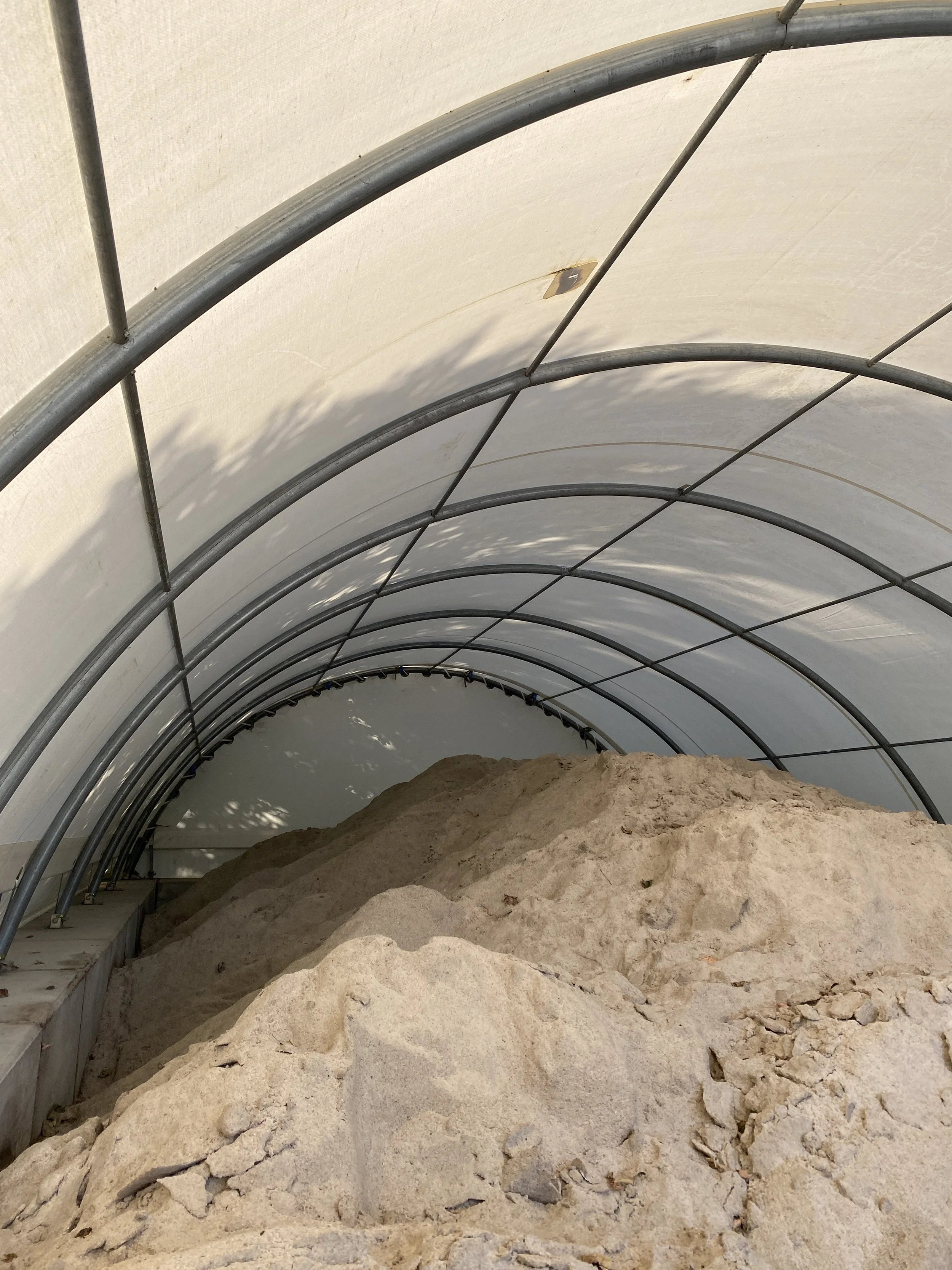 Inside of a fabric barn with a curved metal frame and a pile of salt at the bottom.