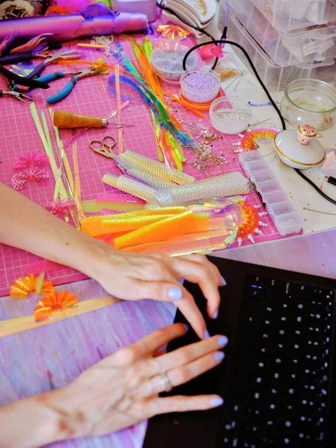 Craft book author typing on laptop next to her colorful work space
