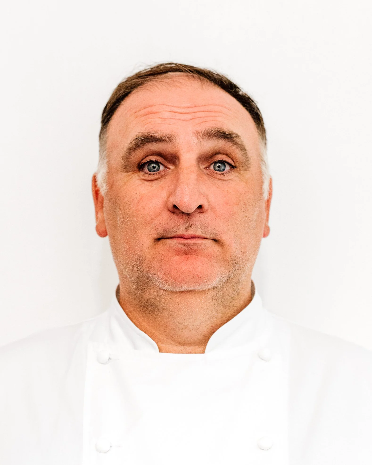 Chef Jose Andres. A professional male chef with short brown hair, blue eyes, and light stubble, wearing a white chef's coat, standing against a plain white background.