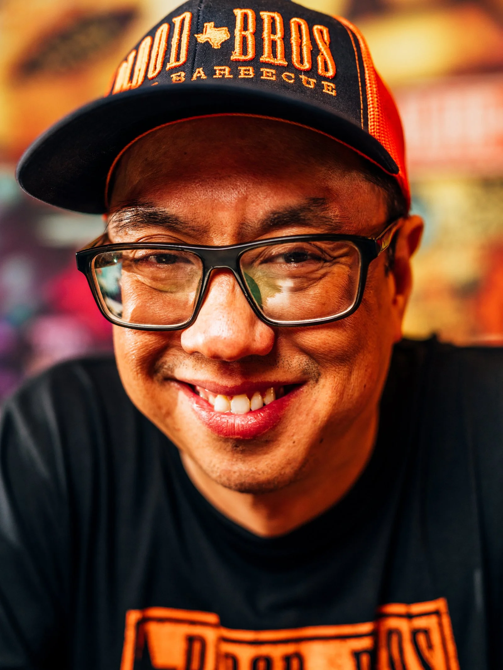 A man wearing a black and orange cap that says 'Old Bros' and 'San Diego' with glasses, smiling at the camera.