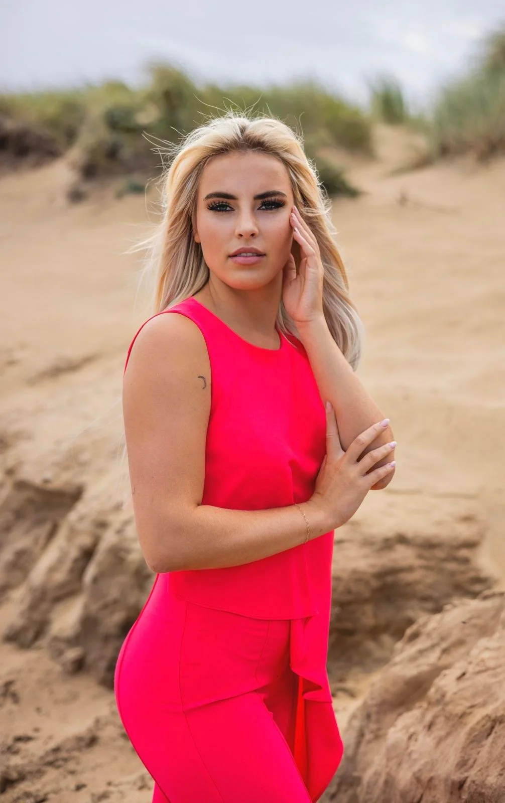 A woman with dark hair and a black dress standing beside a broken glass window with wooden framing, surrounded by greenery and vines.