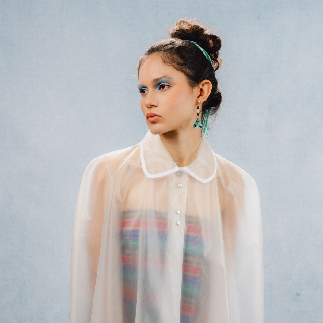 A young woman with long brown hair wearing a yellow blouse with floral details, pink eyeshadow, and natural makeup, looking directly at the camera.