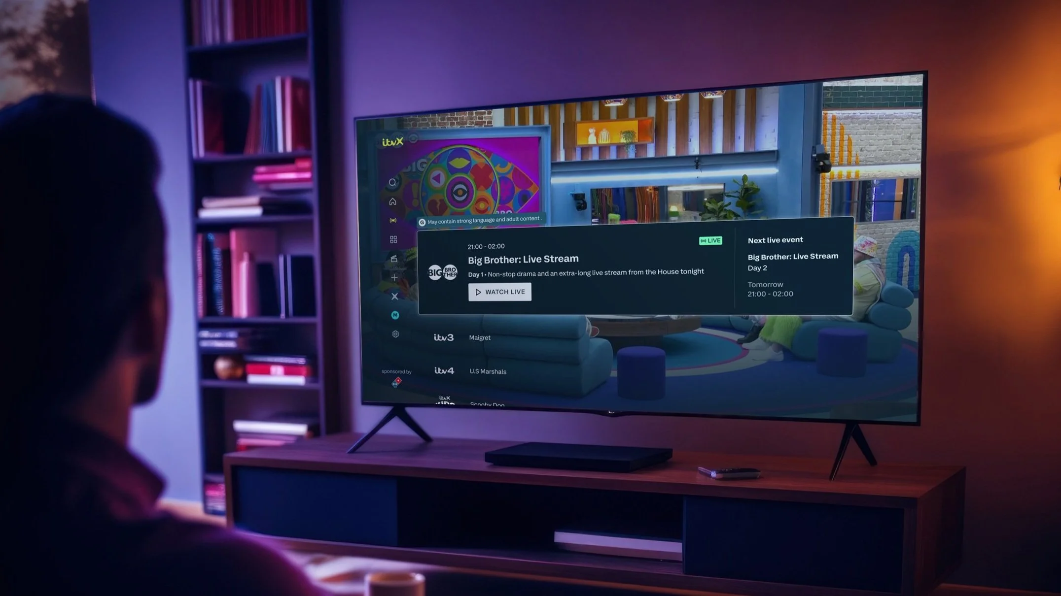 Figure watching TV that displays the electronic programme guide (EPG) featuring the Big Brother Live Stream with the broadcast displayed behind it